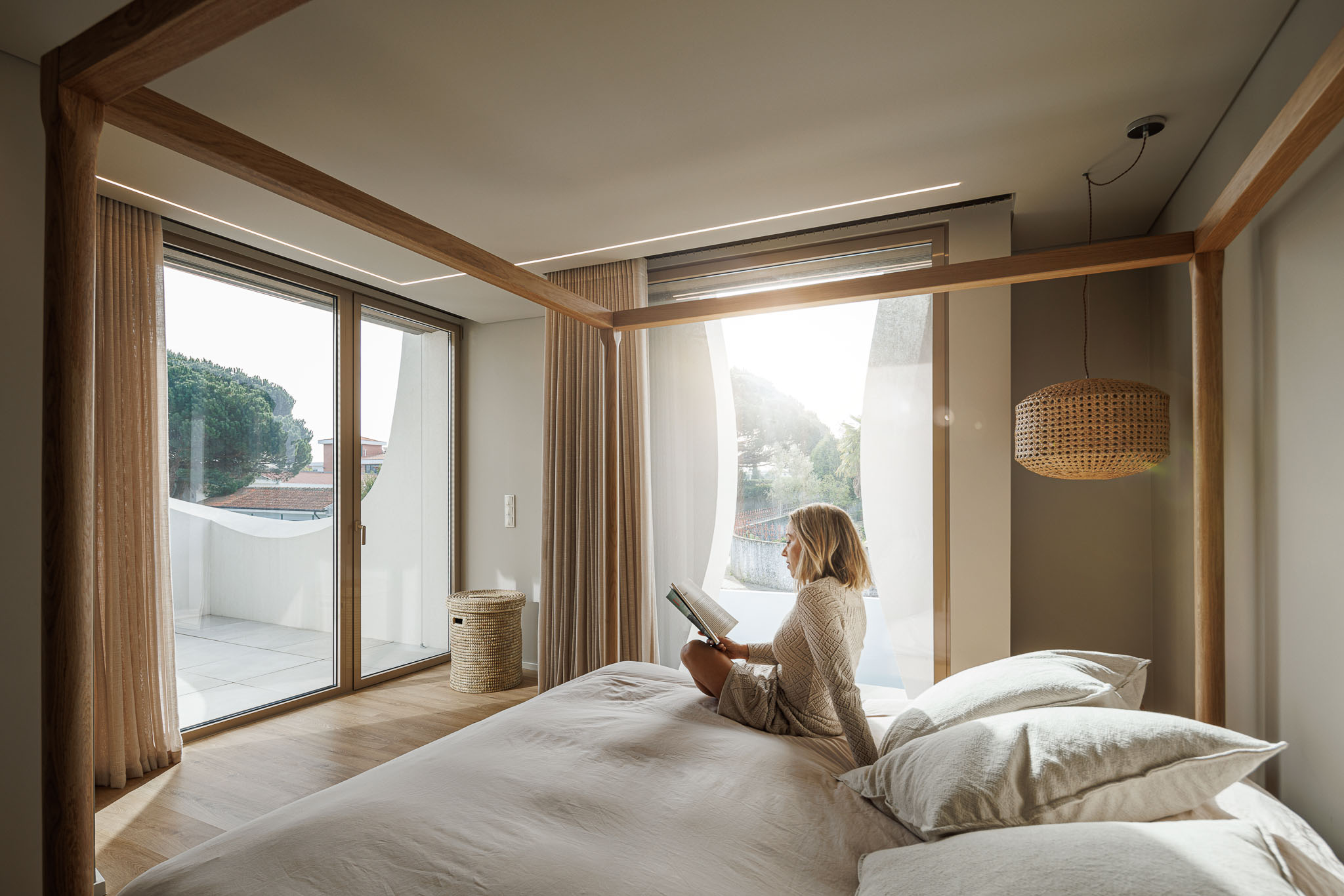 Quarto: Cama de dossel em madeira clara, pavimento em madeira, cortinas claras e varanda com guardas curvas brancas. — Casa Pátios de Pétalas arquitetura Sandra Micaela Casinha Atelier em Gondomar