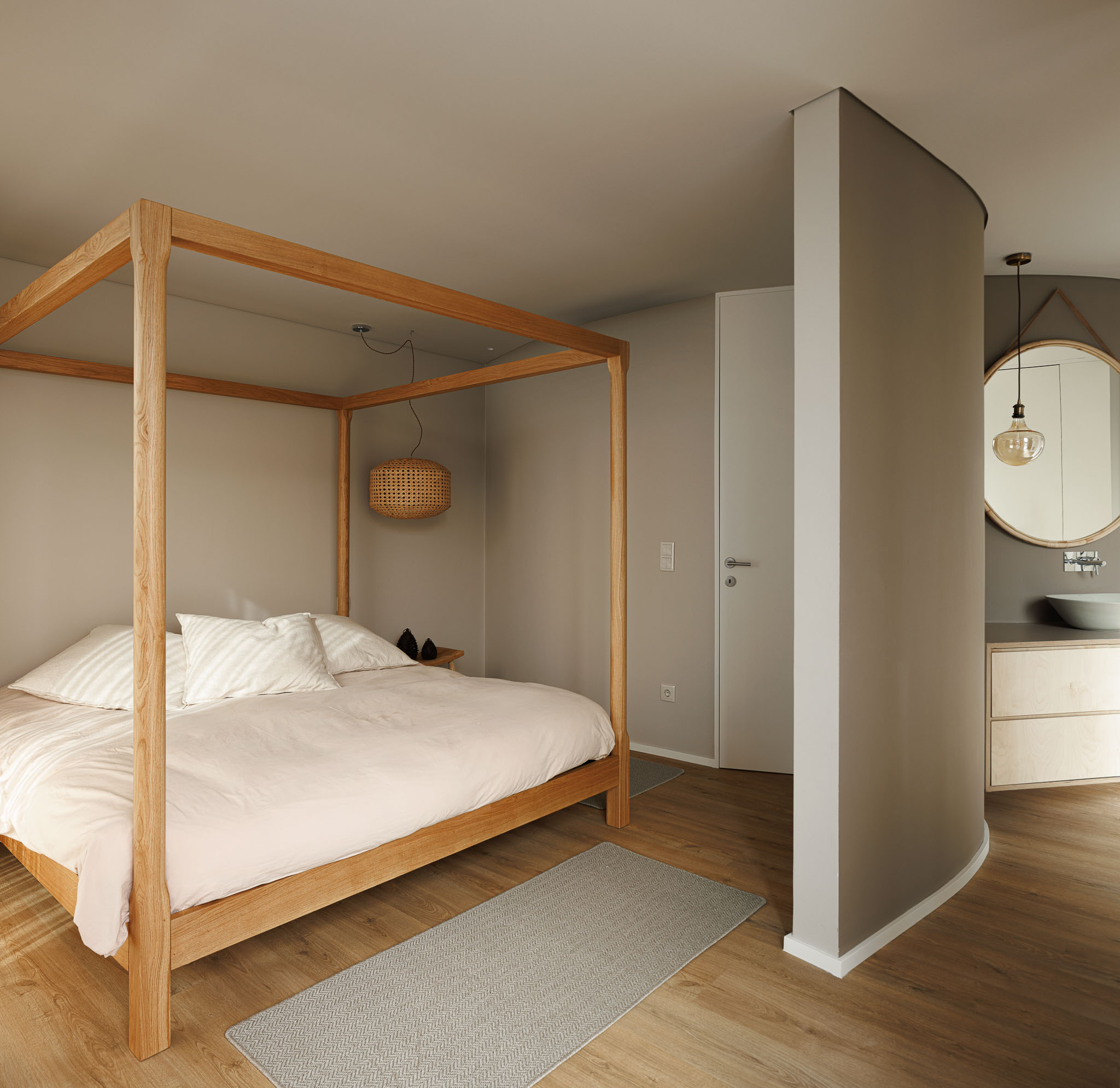 Quarto: Cama de dossel em madeira clara, alcatifa cinzenta e acesso à casa de banho com lavatório circular. — Casa Pátios de Pétalas arquitetura Sandra Micaela Casinha Atelier em Gondomar
