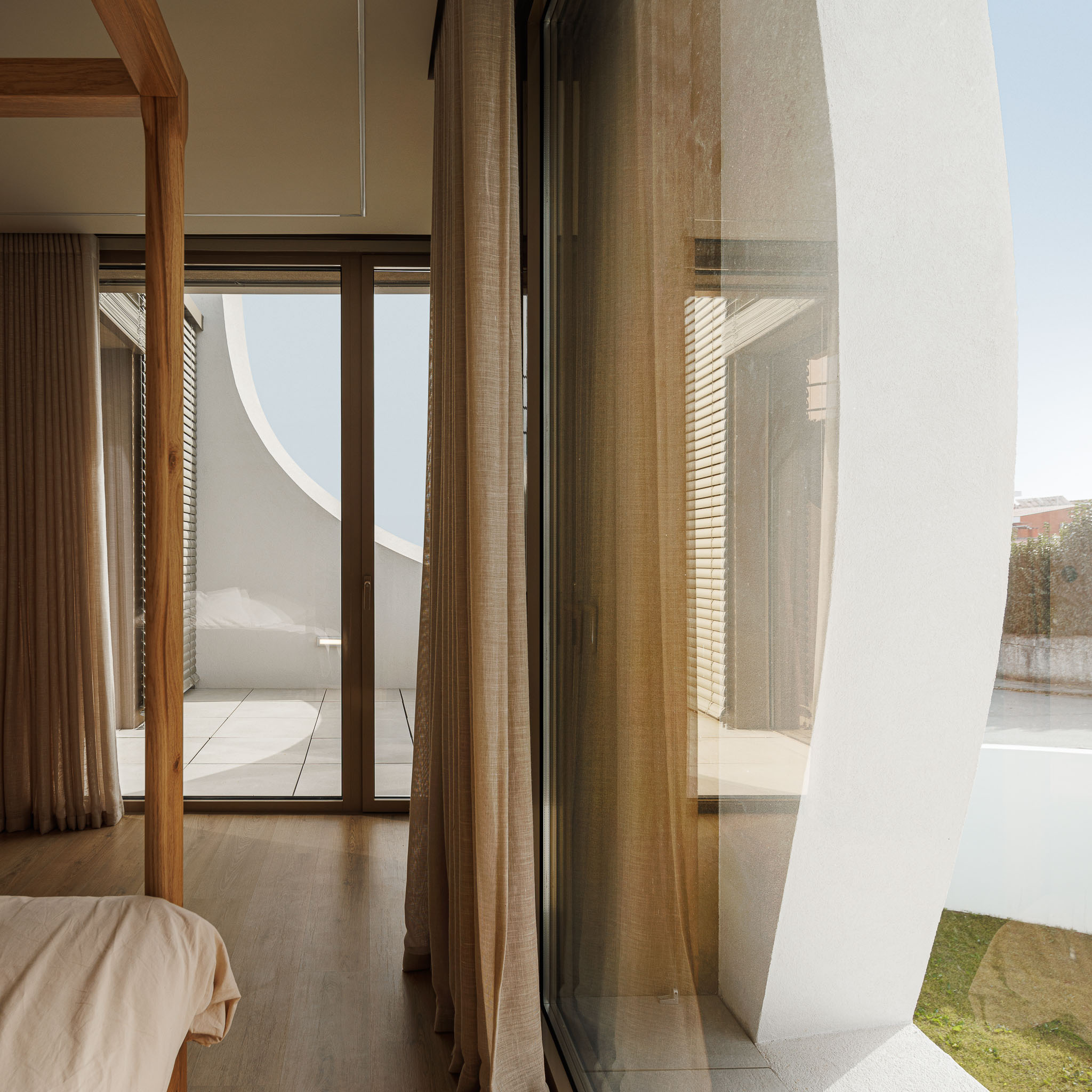 Quarto: Detalhe da varanda curva branca, cortinas claras e cama de dossel em madeira. — Casa Pátios de Pétalas arquitetura Sandra Micaela Casinha Atelier em Gondomar