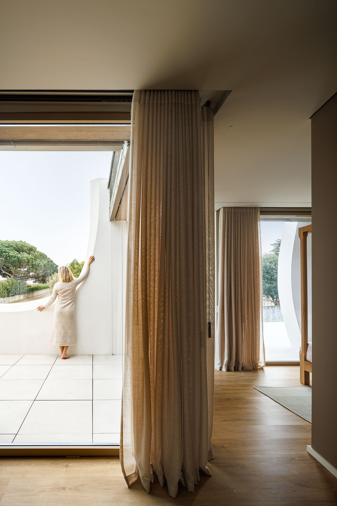 Quarto: Vista da varanda com guardas curvas brancas, pavimento cerâmico e cortinas claras. — Casa Pátios de Pétalas arquitetura Sandra Micaela Casinha Atelier em Gondomar