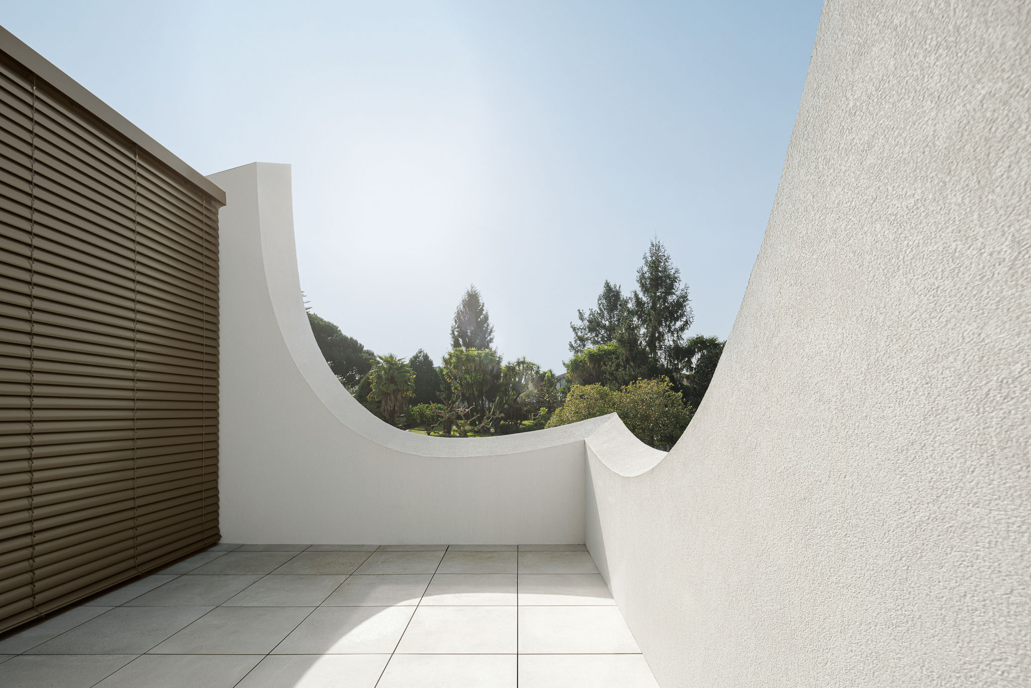 Varanda: Guarda curva branca com ripas horizontais e pavimento cerâmico. — Casa Pátios de Pétalas arquitetura Sandra Micaela Casinha Atelier em Gondomar