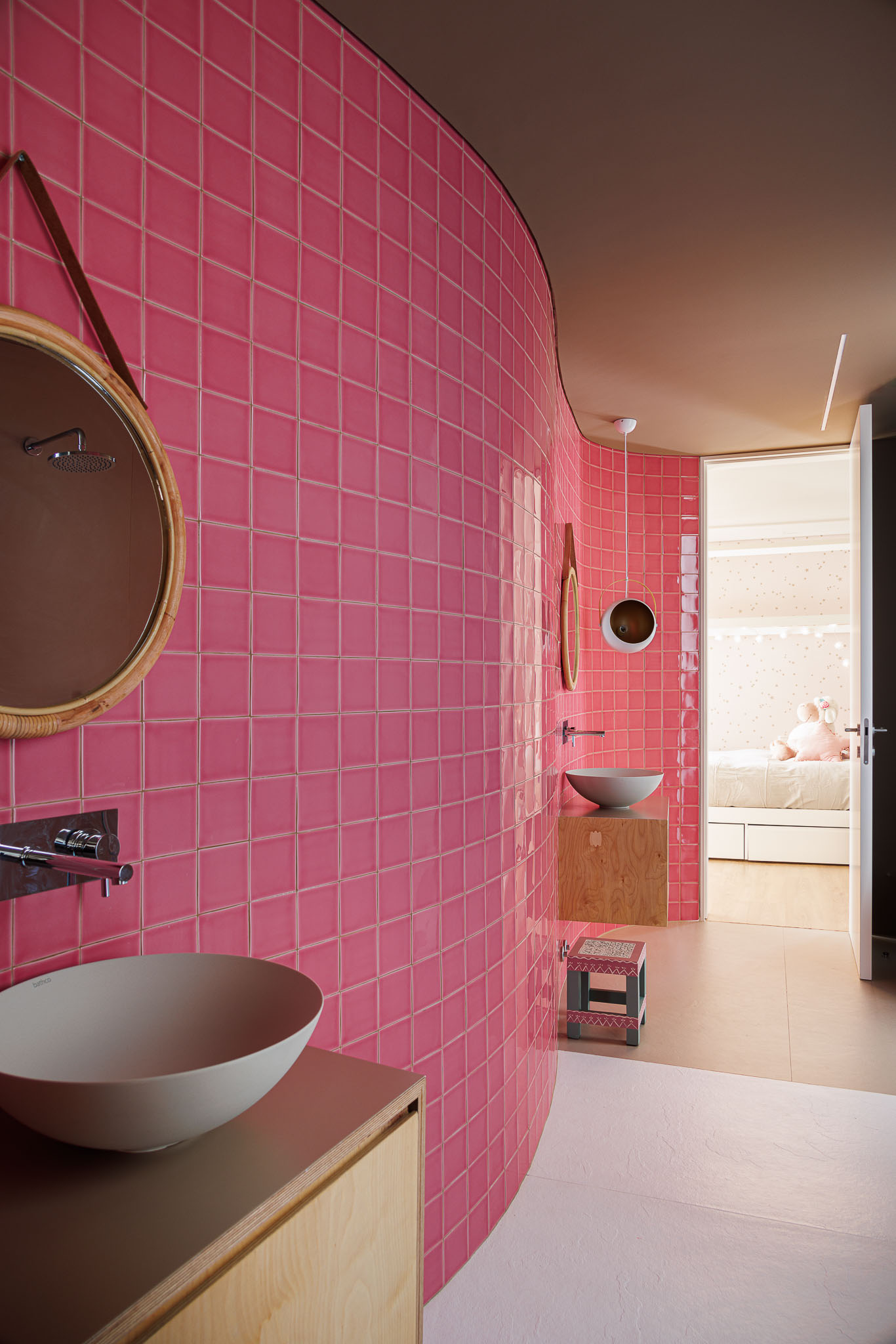 Casa de banho infantil: Azulejos rosa, lavatório circular, espelho com moldura em vime e pavimento rosa e branco. — Casa Pátios de Pétalas arquitetura Sandra Micaela Casinha Atelier em Gondomar