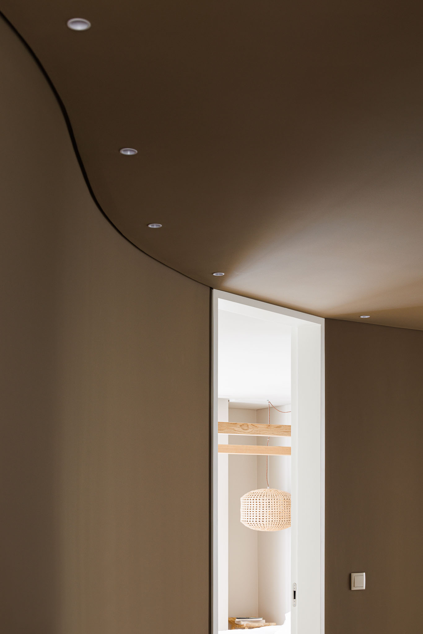 Corredor: Detalhe da parede curva em tons terra e candeeiro de vime suspenso. — Casa Pátios de Pétalas arquitetura Sandra Micaela Casinha Atelier em Gondomar