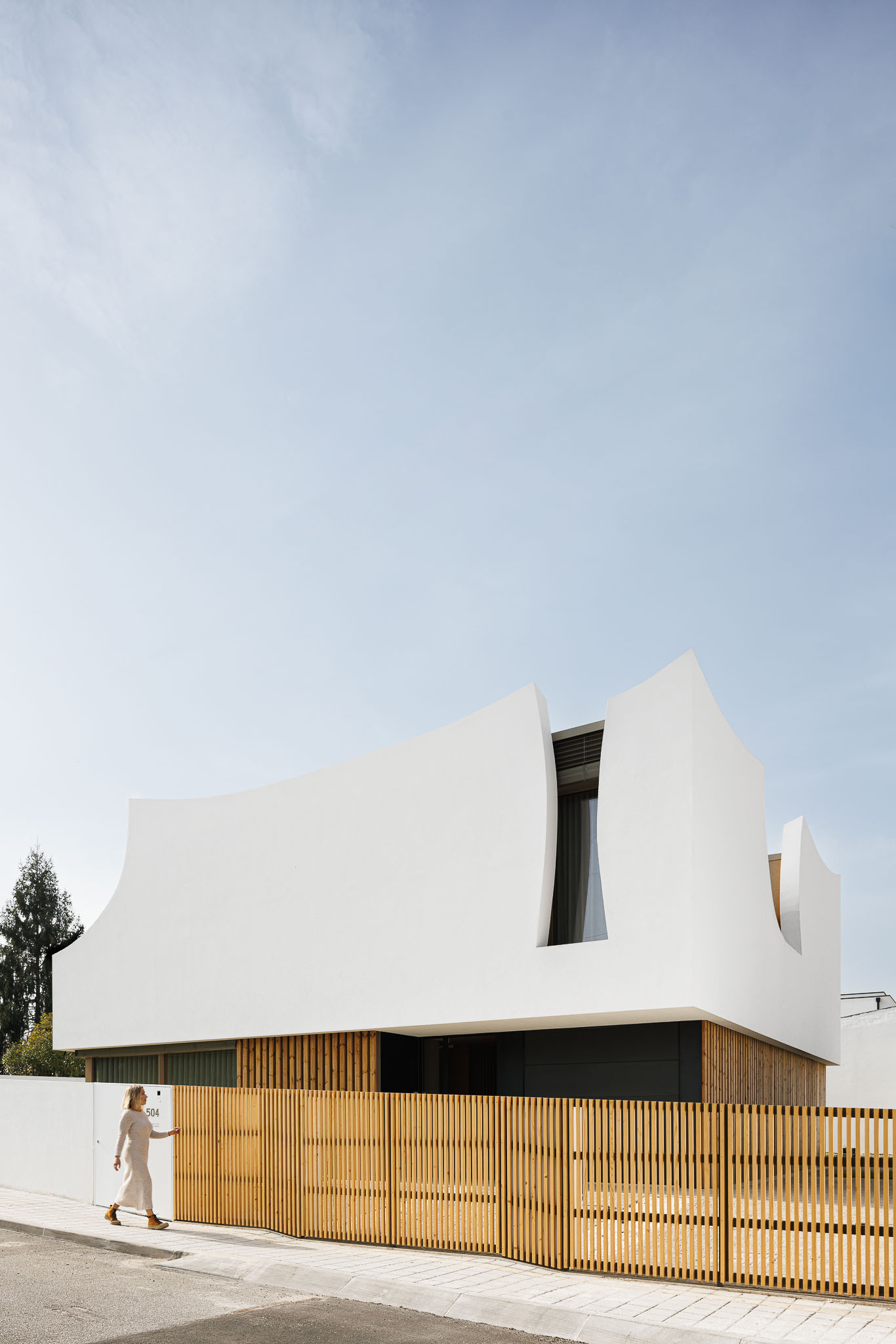 Exterior: Vista frontal da casa com fachada branca, detalhes curvos e vedação em madeira. — Casa Pátios de Pétalas arquitetura Sandra Micaela Casinha Atelier em Gondomar