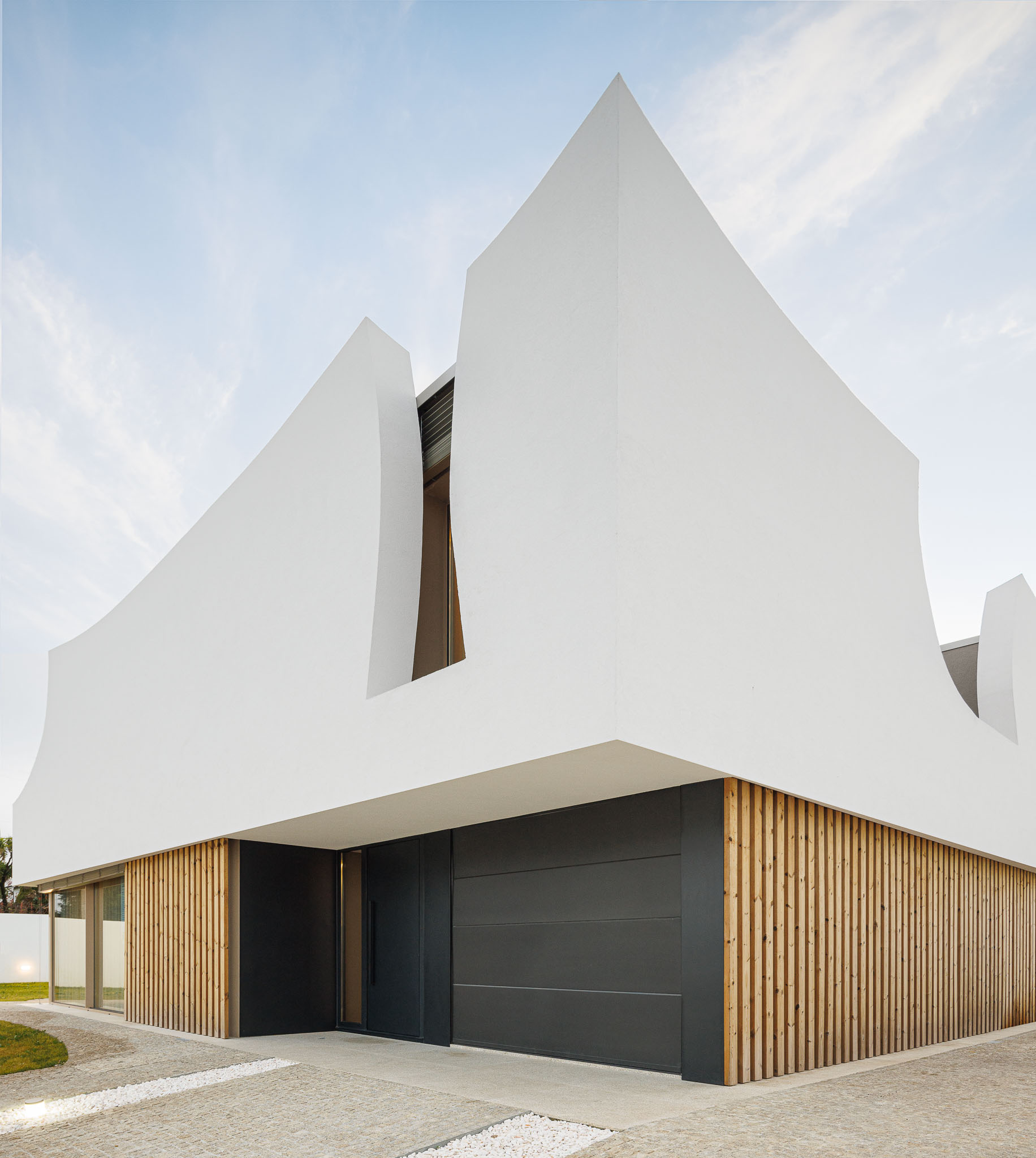 Exterior: Fachada da casa com detalhes curvos, revestimento em madeira e porta de garagem. — Casa Pátios de Pétalas arquitetura Sandra Micaela Casinha Atelier em Gondomar