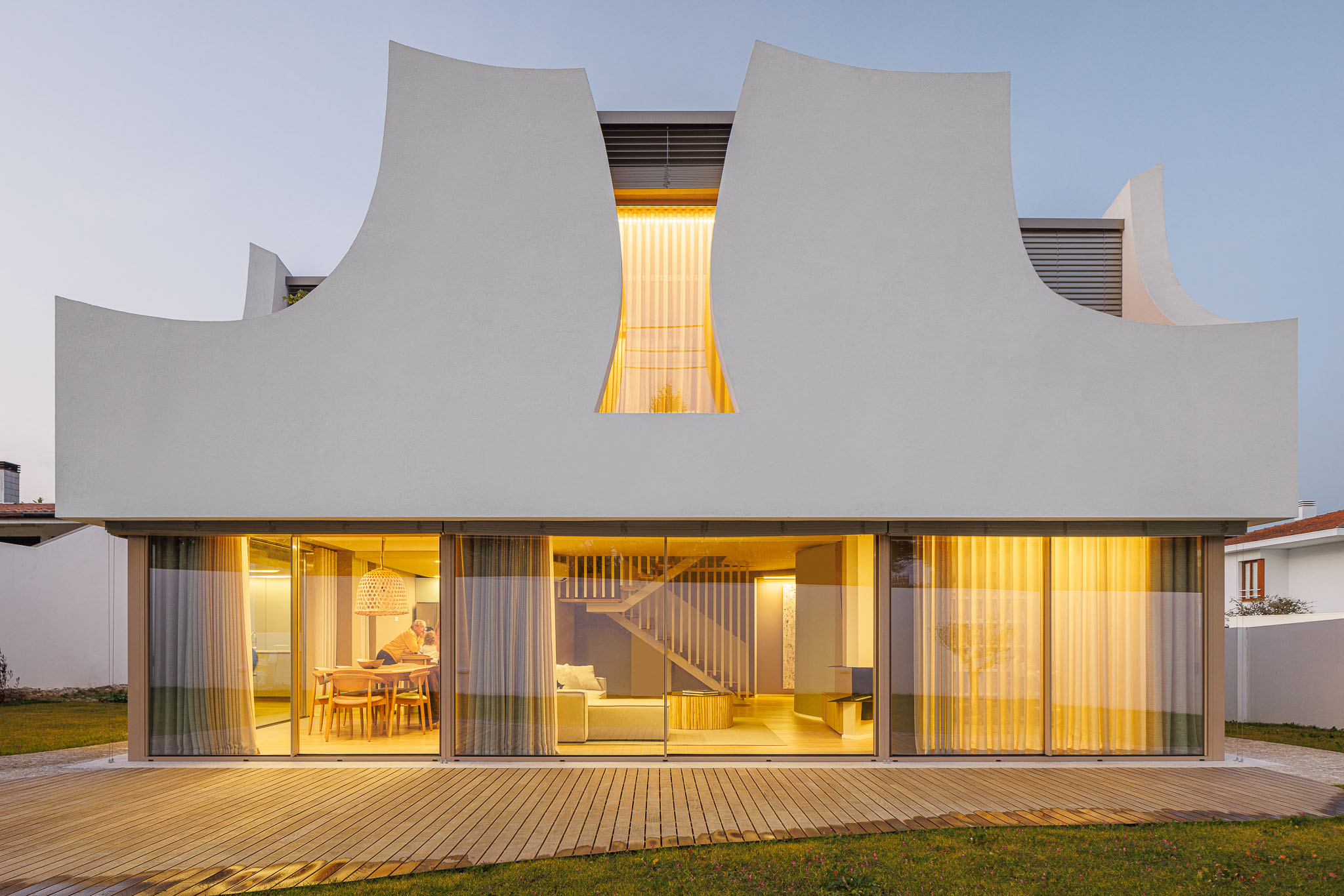 Exterior: Fachada da casa com detalhes curvos e janelas iluminadas. — Casa Pátios de Pétalas arquitetura Sandra Micaela Casinha Atelier em Gondomar
