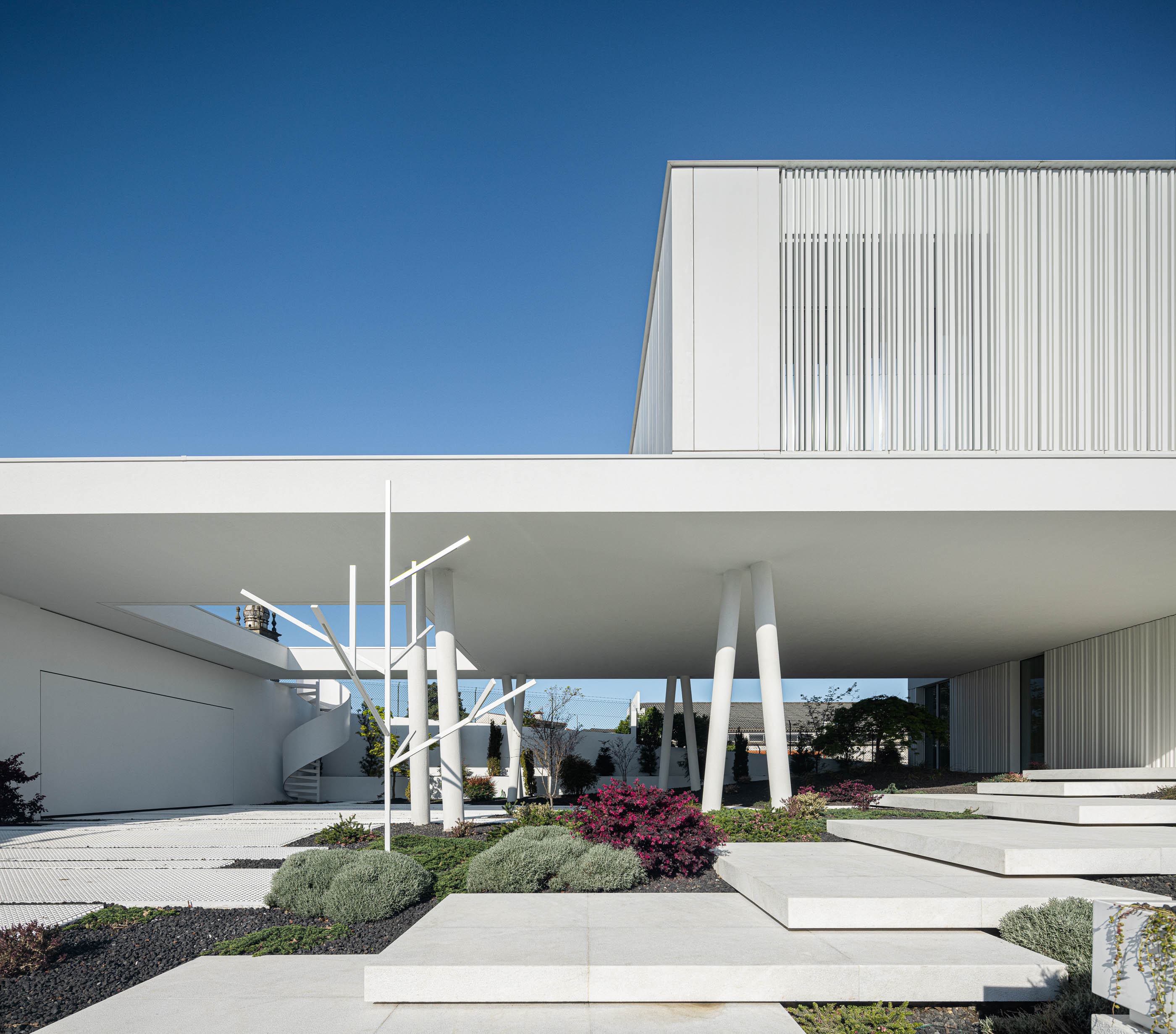 Jardim: Vista da moradia com jardim minimalista, escada em caracol e passagens em pedra. — Riscowhite arquitetura Risco Singular em Barcelos
