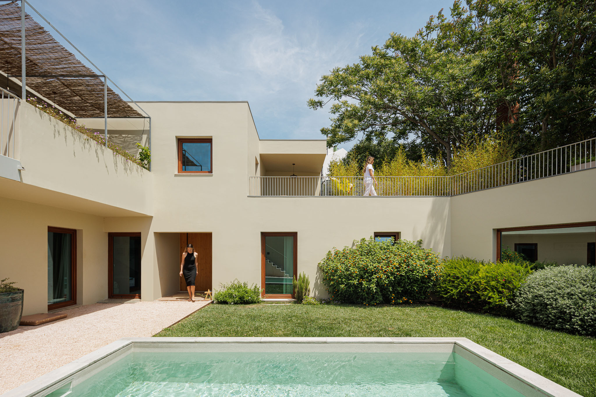 Exterior: Fachada minimalista em tons neutros, com piscina, relvado e gravilha. Varandas com guarda-corpos metálicos e cobertura de colmo. — Prazeres 37 arquitetura Fragmentos em Lisboa