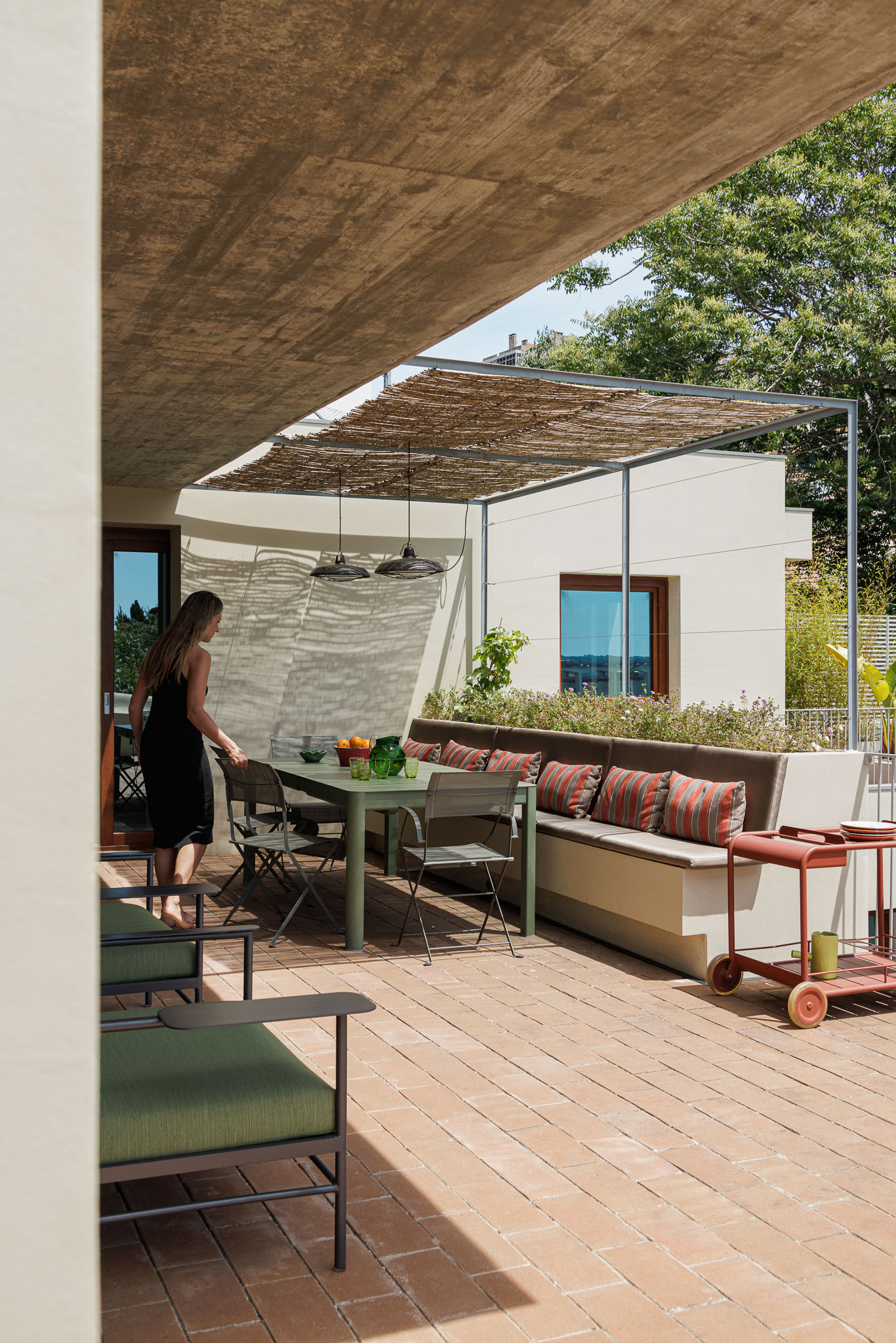 Terraço: Espaço exterior com pavimento em tijoleira, toldo de colmo, mesa de refeições e sofás com almofadas coloridas. — Prazeres 37 arquitetura Fragmentos em Lisboa