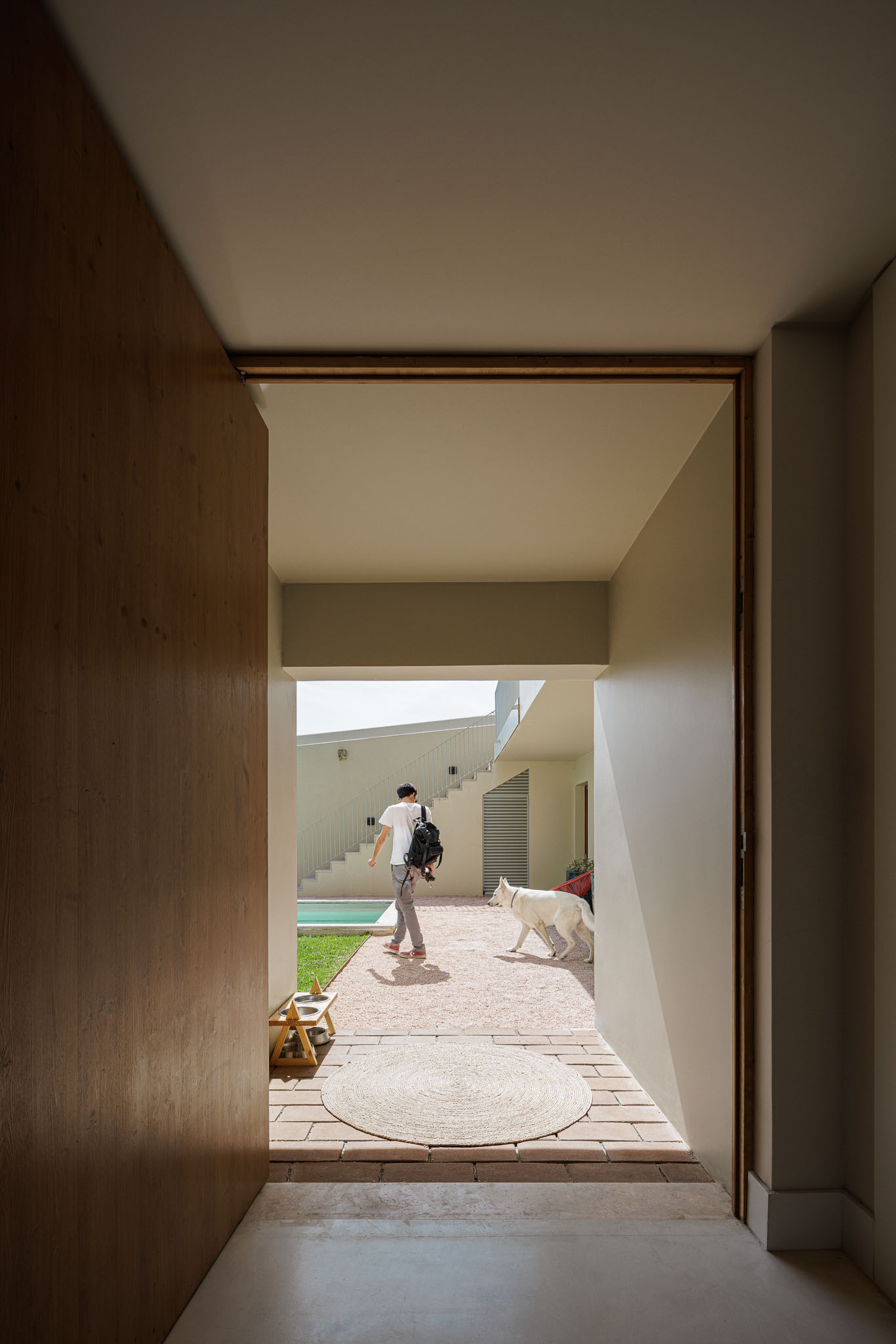 Entrada: Porta de madeira maciça, pavimento em tijoleira e tapete de juta. Vista para o pátio interior com piscina e escadas. — Prazeres 37 arquitetura Fragmentos em Lisboa