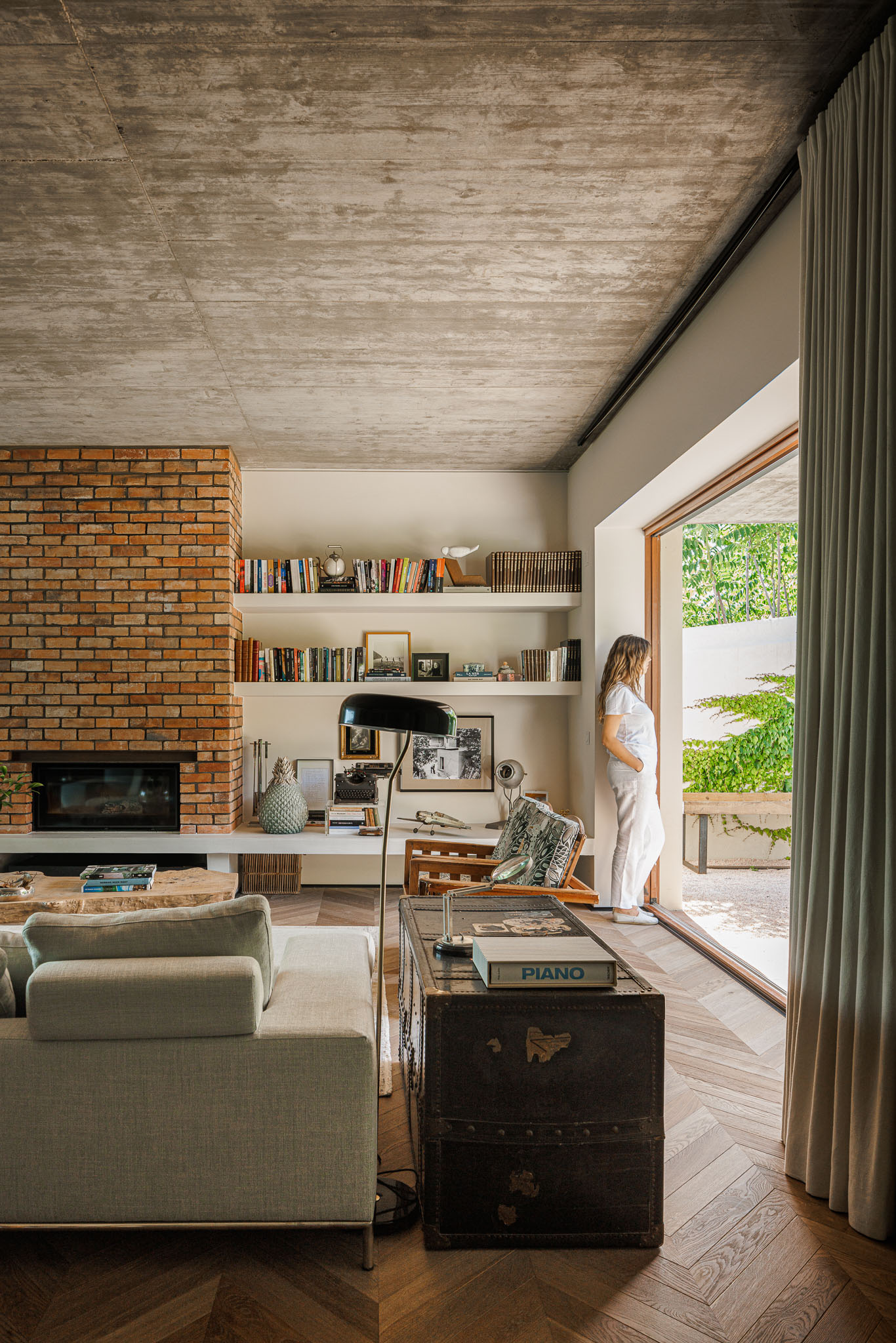 Sala de estar: Lareira em tijolo rústico, estantes embutidas e pavimento em espinha de peixe. Sofá cinzento e vista para o jardim. — Prazeres 37 arquitetura Fragmentos em Lisboa