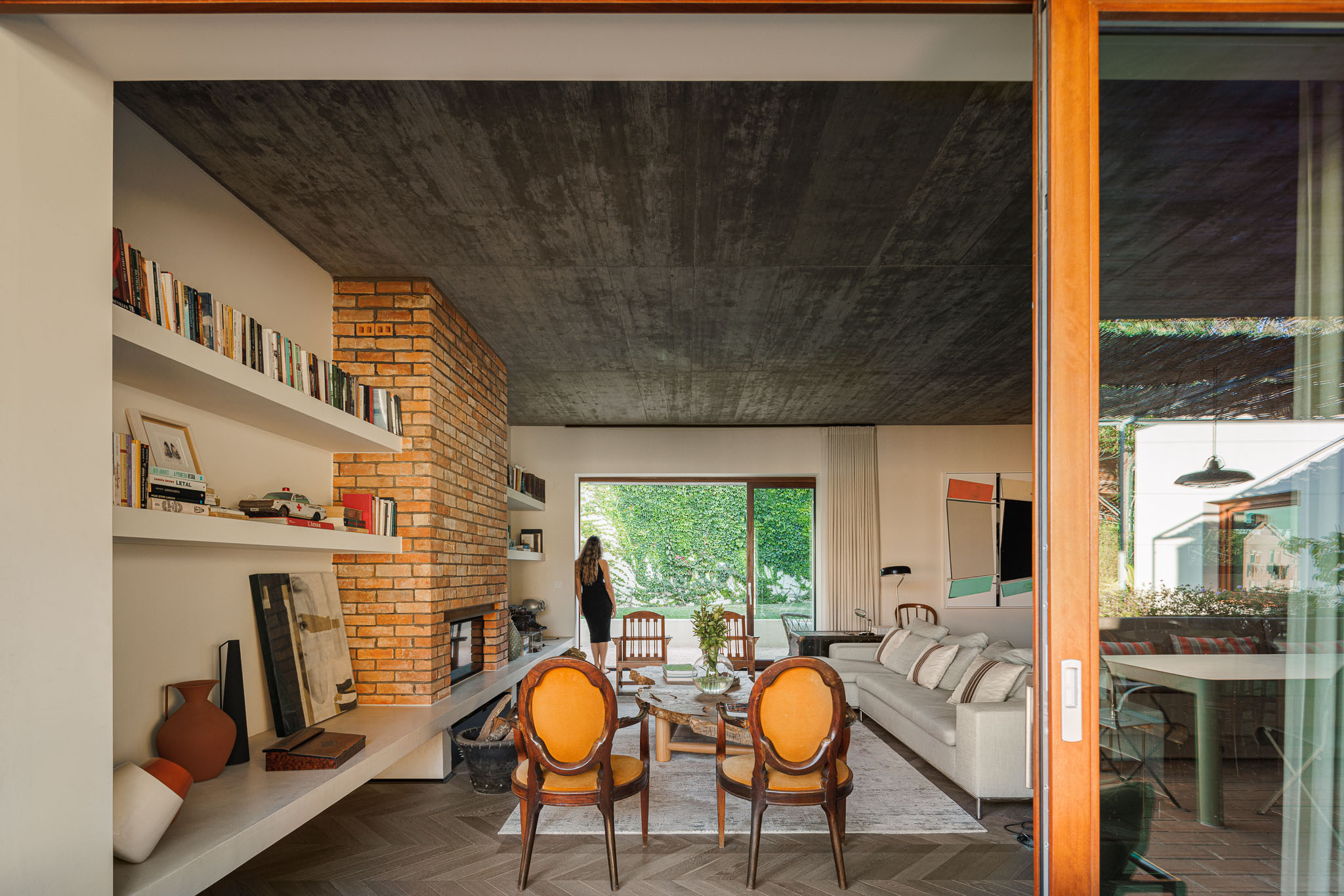 Sala de estar: Espaço amplo com lareira em tijolo, sofás confortáveis e pavimento em madeira. Acesso ao terraço e jardim. — Prazeres 37 arquitetura Fragmentos em Lisboa
