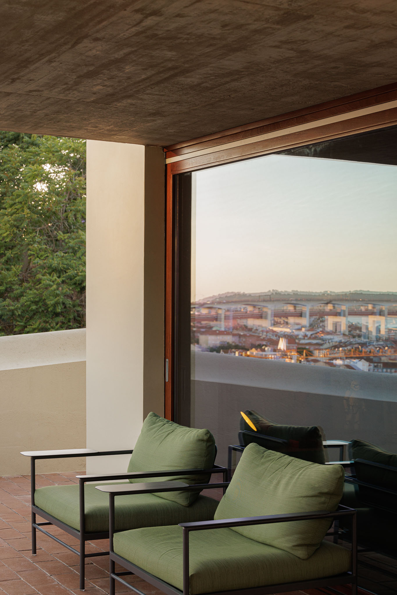 Terraço: Cadeiras de exterior com almofadas verdes e vista panorâmica sobre a cidade de Lisboa. Pavimento em tijoleira. — Prazeres 37 arquitetura Fragmentos em Lisboa