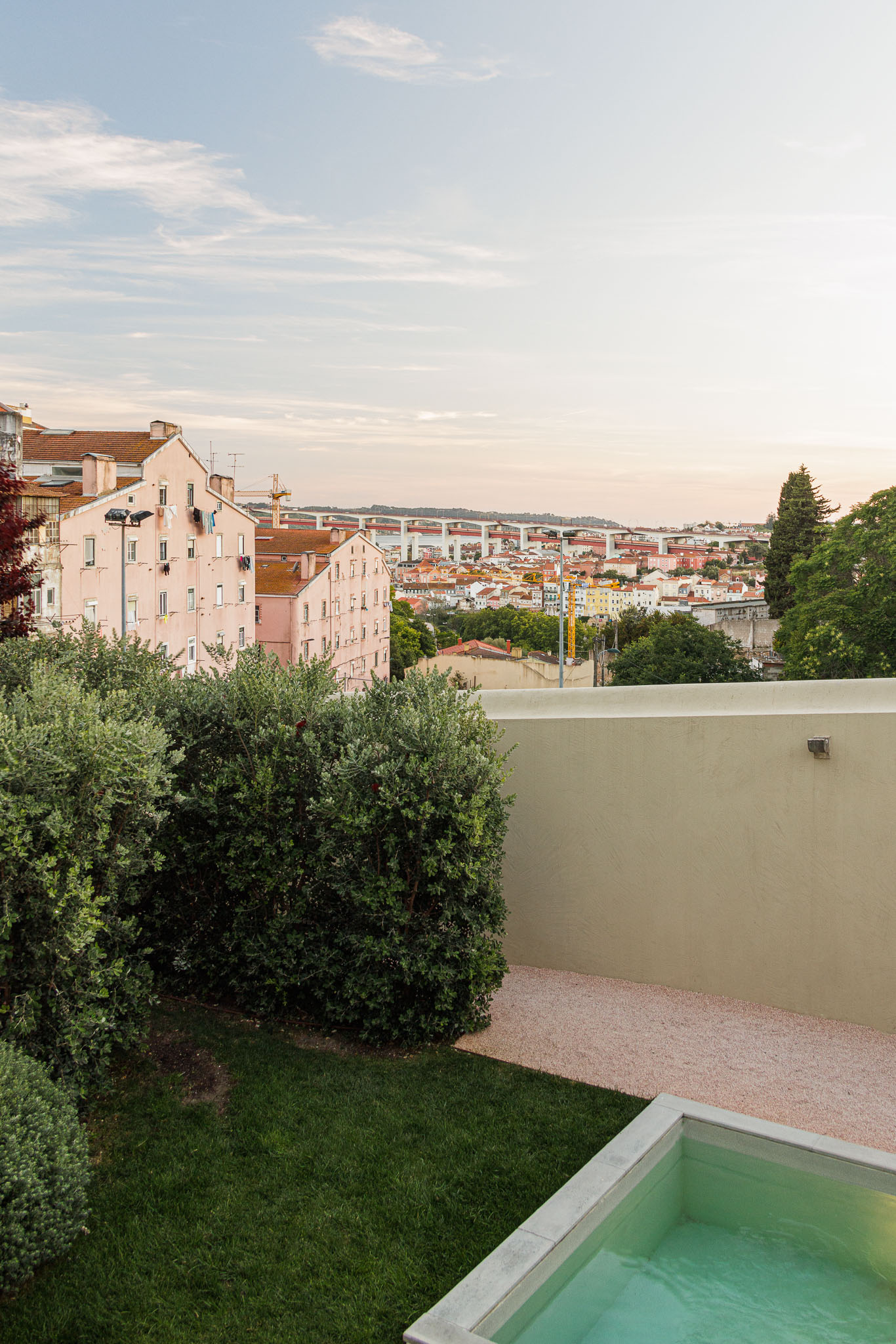 Exterior: Piscina com borda em betão, relvado e vegetação. Vista para a cidade de Lisboa e edifícios históricos. — Prazeres 37 arquitetura Fragmentos em Lisboa