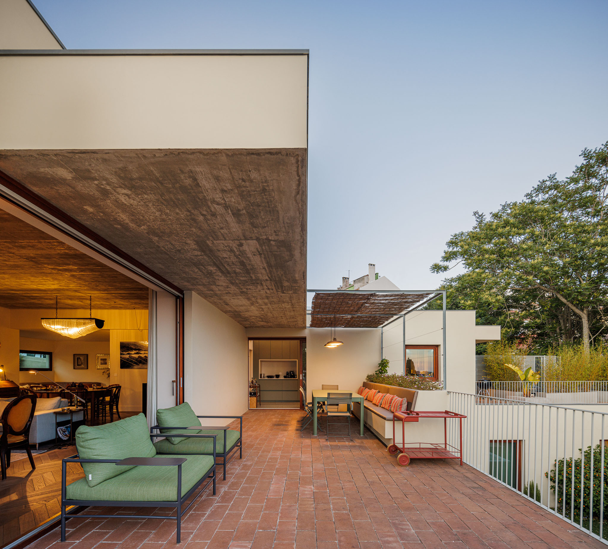 Terraço: Espaço exterior com pavimento em tijoleira, sofás, mesa de refeições e vista para a sala de estar e jardim. — Prazeres 37 arquitetura Fragmentos em Lisboa
