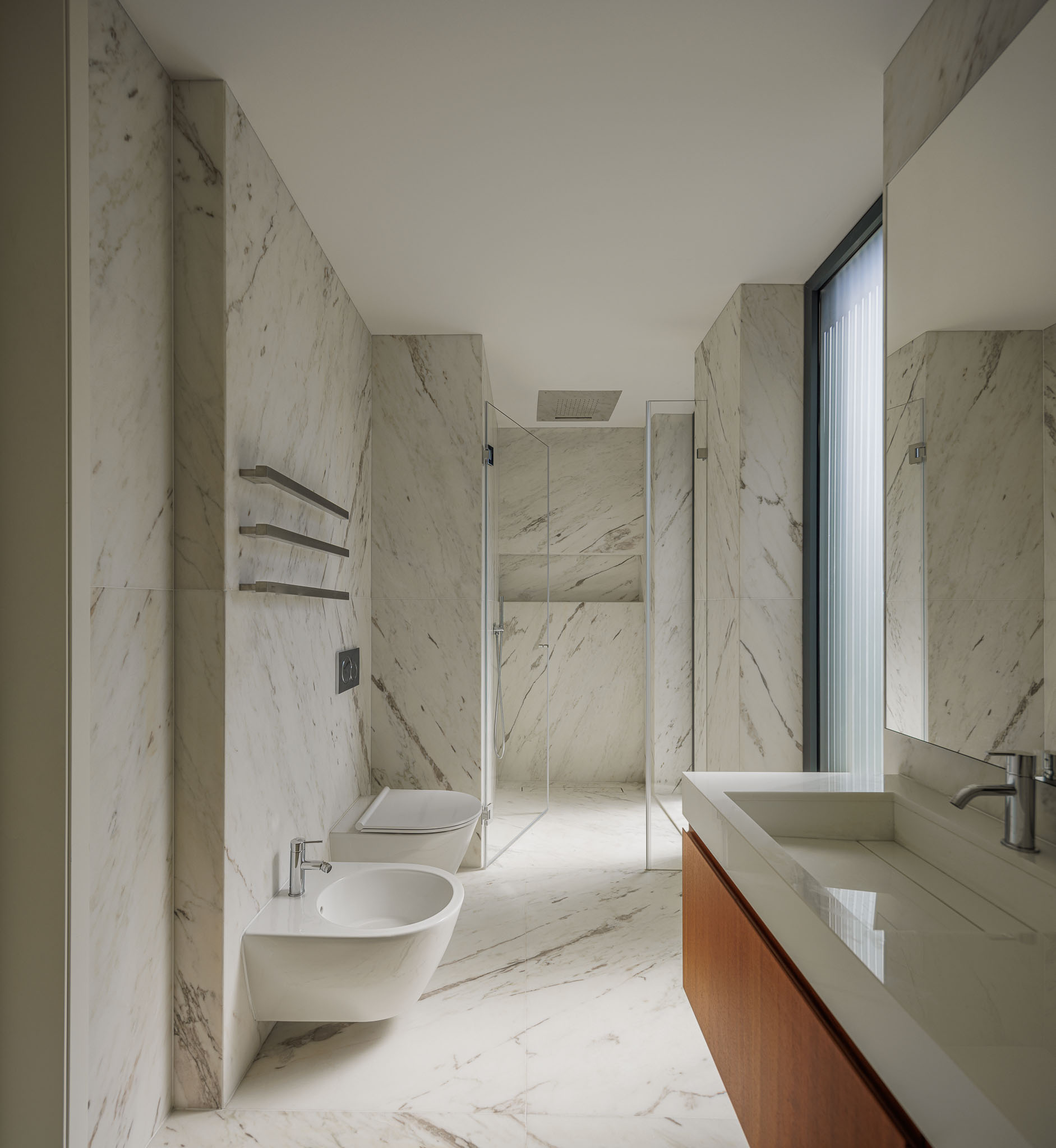 Casa de banho: Revestimento em mármore branco, duche em vidro, lavatório embutido em bancada de madeira. Estilo minimalista. — CONCRETE 11 arquitetura Cage Atelier em Lisboa