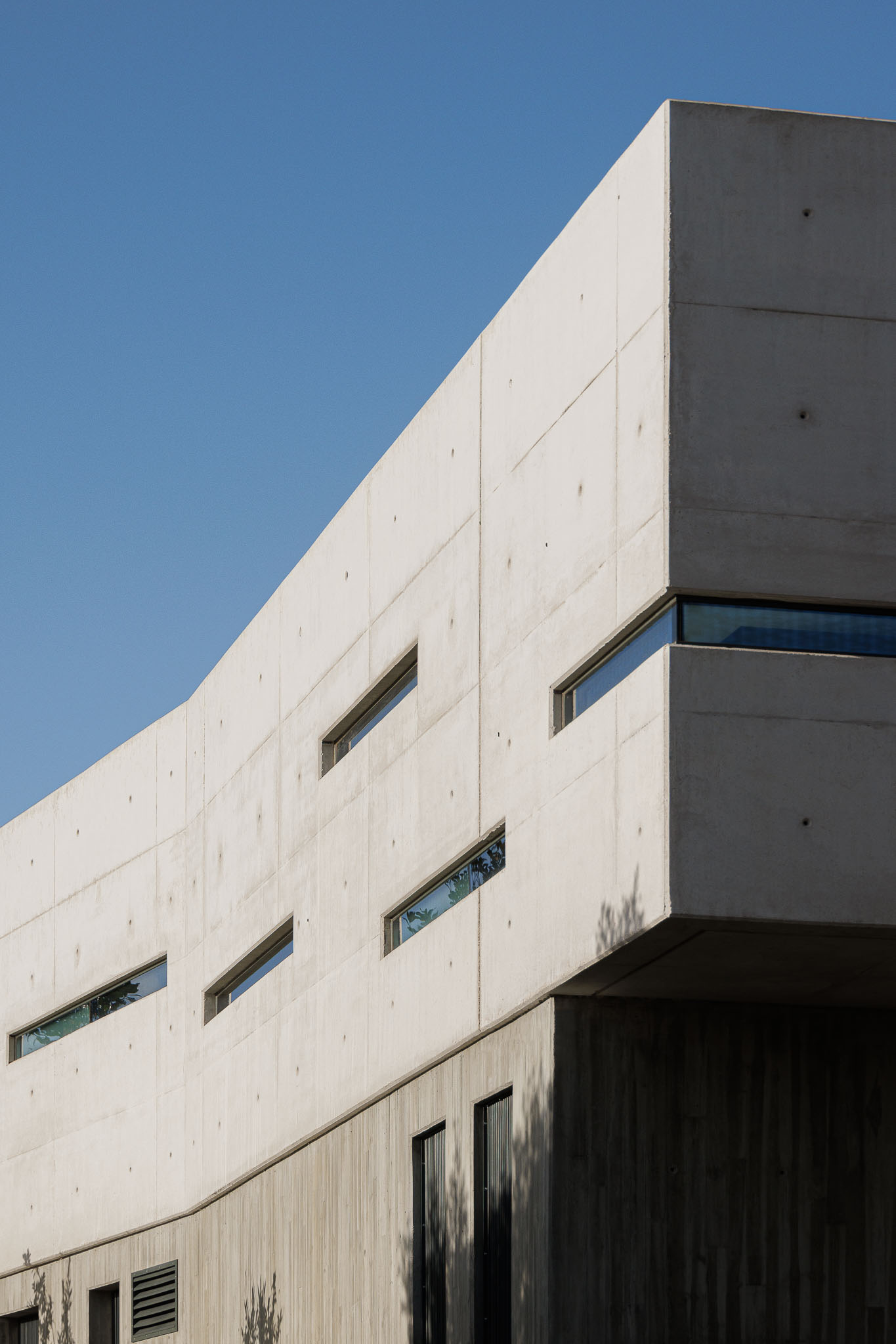Exterior: Detalhe da fachada em betão com janelas estreitas e geométricas, sob céu azul. — CONCRETE 11 arquitetura Cage Atelier em Lisboa