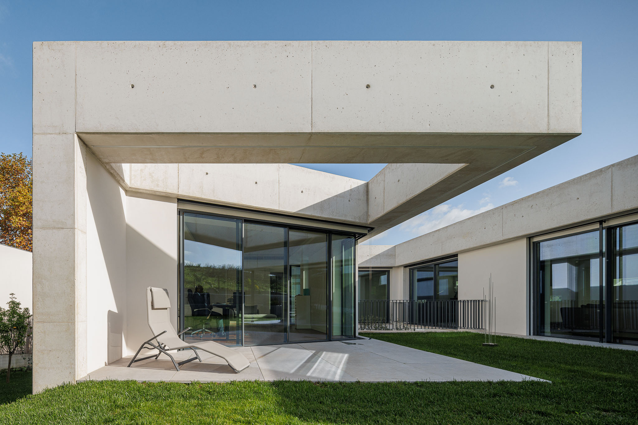 Exterior: Alpendre em betão com cadeiras de descanso, porta de correr envidraçada e jardim. — CONCRETE 11 arquitetura Cage Atelier em Lisboa