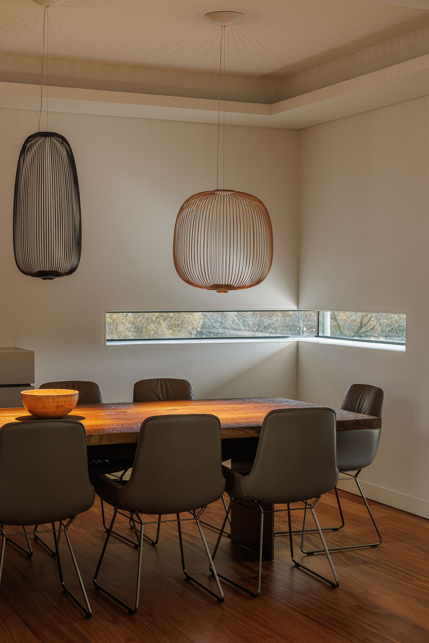 Sala de jantar: Mesa de madeira maciça com cadeiras de couro, candeeiros suspensos e janela horizontal. — CONCRETE 11 arquitetura Cage Atelier em Lisboa