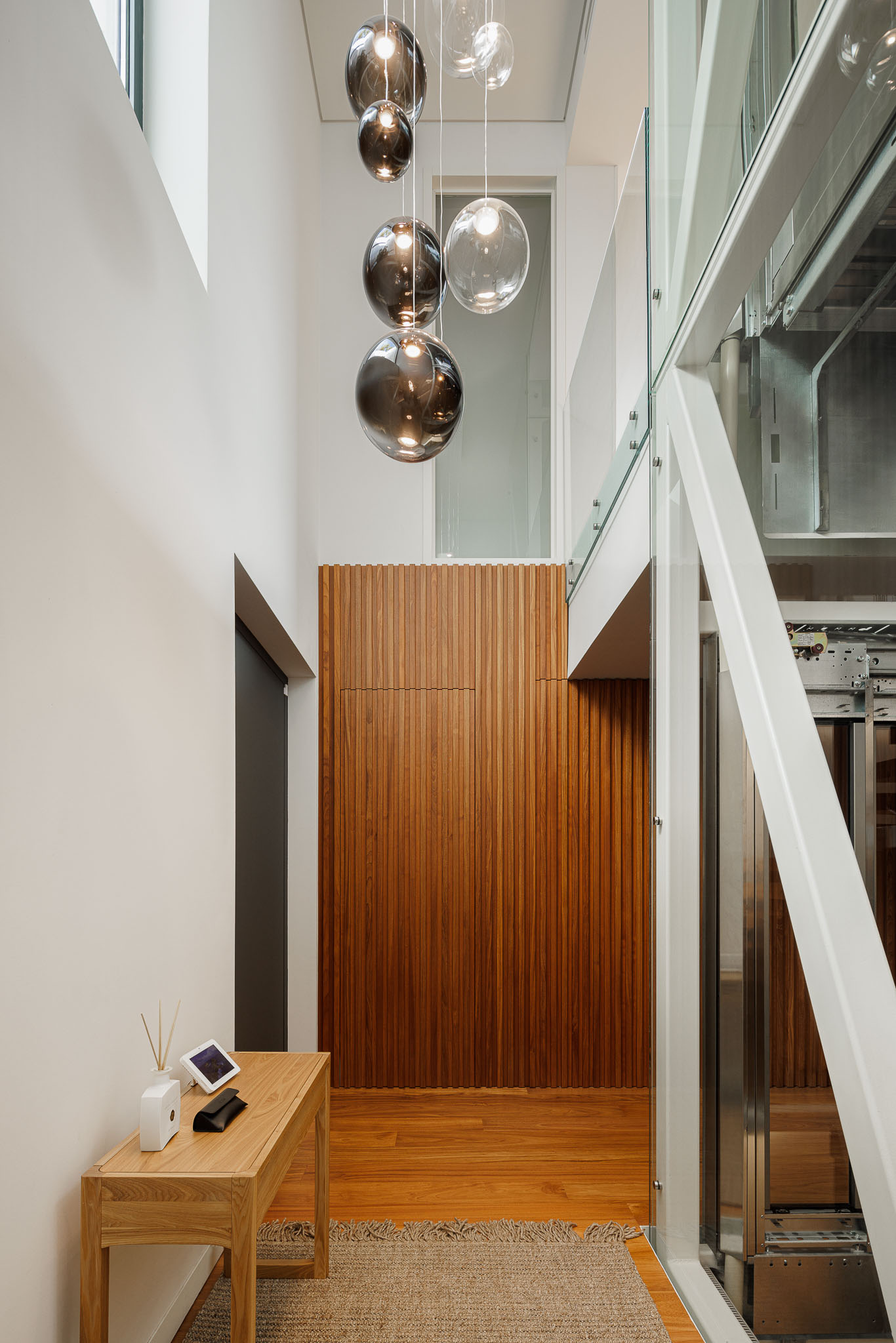 Hall de entrada: Escada e elevador com estrutura metálica e painéis de madeira. Candeeiro de teto com esferas. — CONCRETE 11 arquitetura Cage Atelier em Lisboa