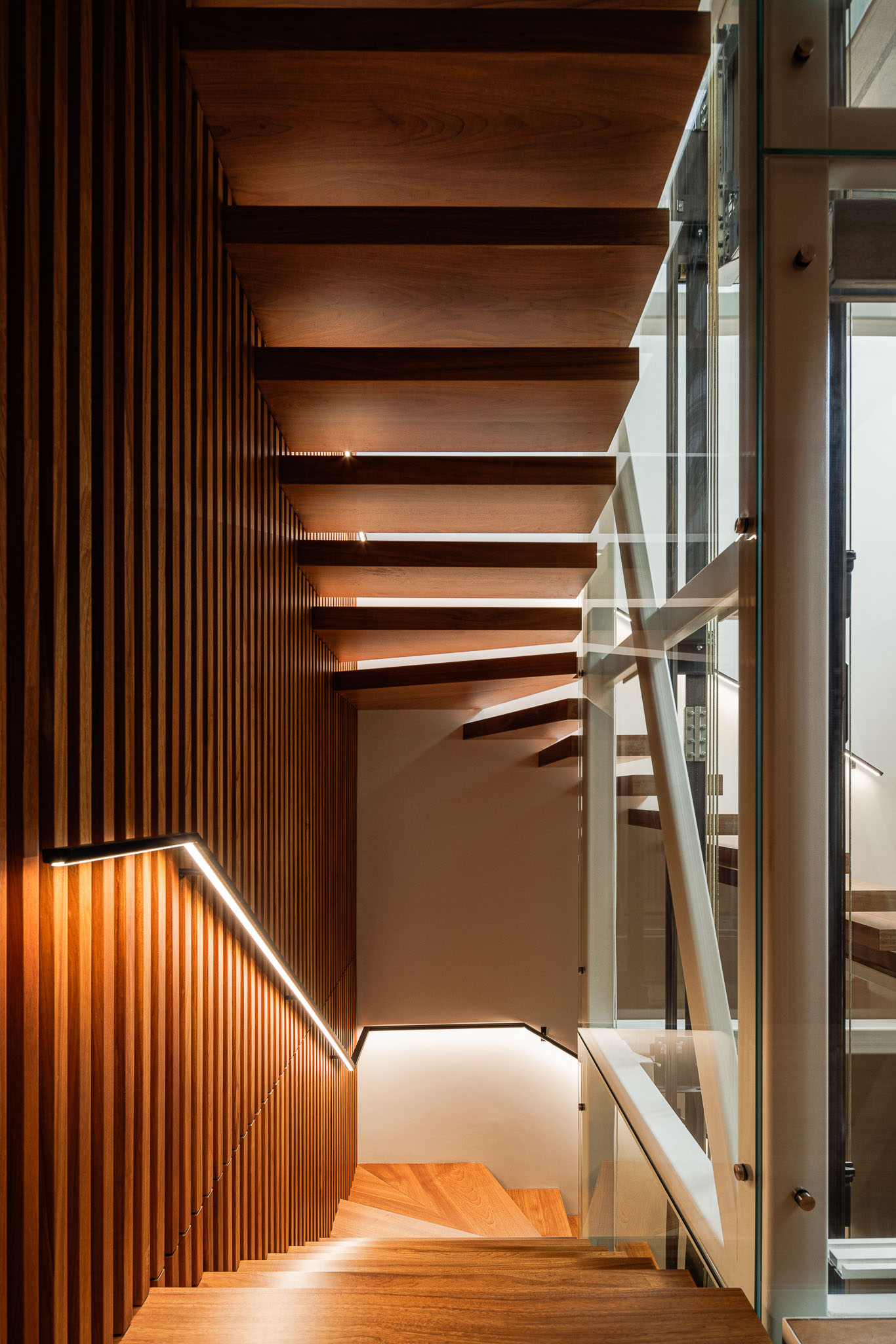 Escada: Degraus de madeira maciça com iluminação embutida e painéis verticais de madeira na parede. — CONCRETE 11 arquitetura Cage Atelier em Lisboa