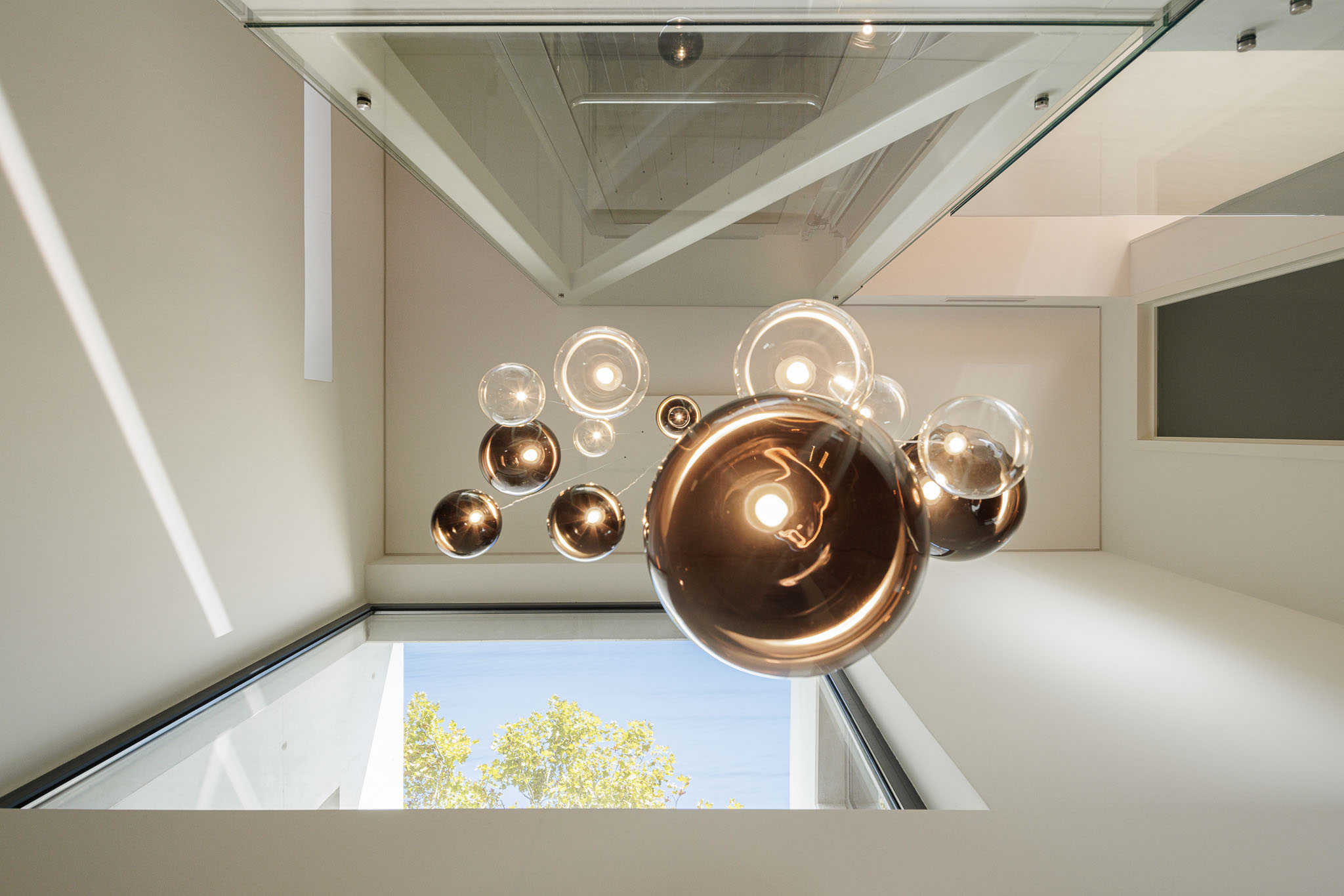 Hall de entrada: Candeeiro de teto com esferas de vidro, escada e claraboia com vista para o céu. — CONCRETE 11 arquitetura Cage Atelier em Lisboa