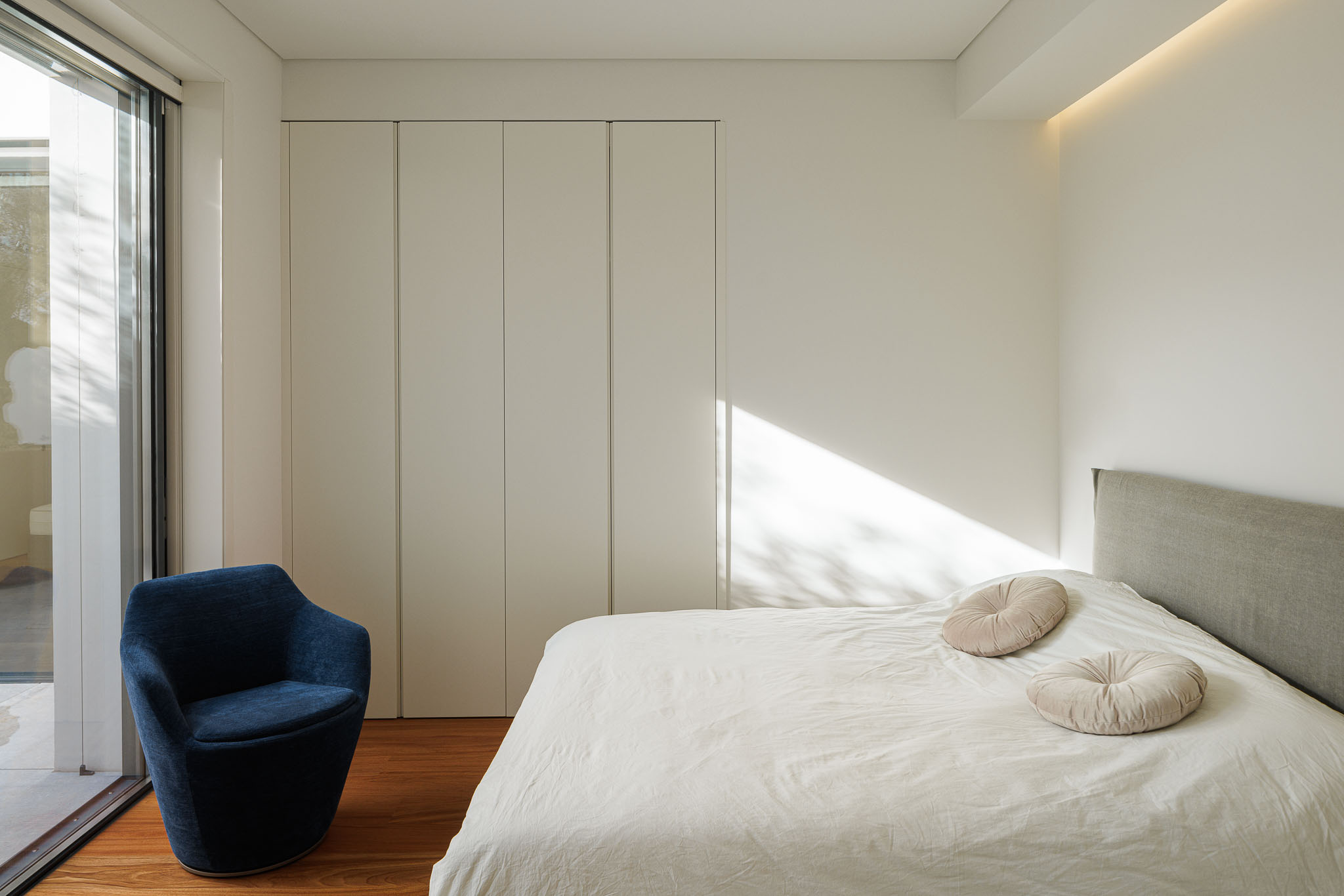 Quarto: Cama com roupa de cama branca, almofadas redondas, armário embutido e janela para o exterior. Pavimento em madeira. — CONCRETE 11 arquitetura Cage Atelier em Lisboa