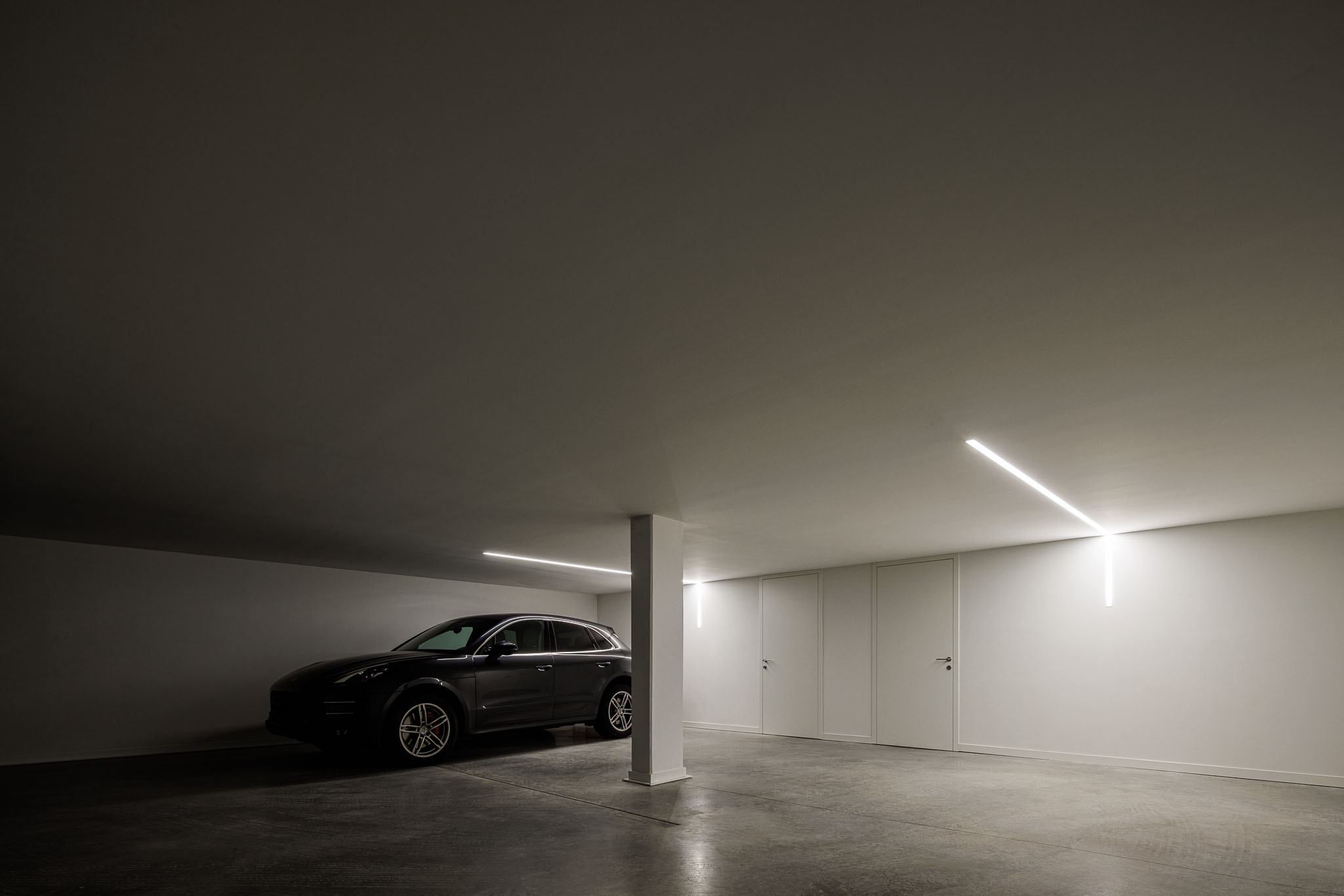 Garagem: Espaço amplo com pavimento em betão, carro estacionado e iluminação linear no teto. — CONCRETE 11 arquitetura Cage Atelier em Lisboa