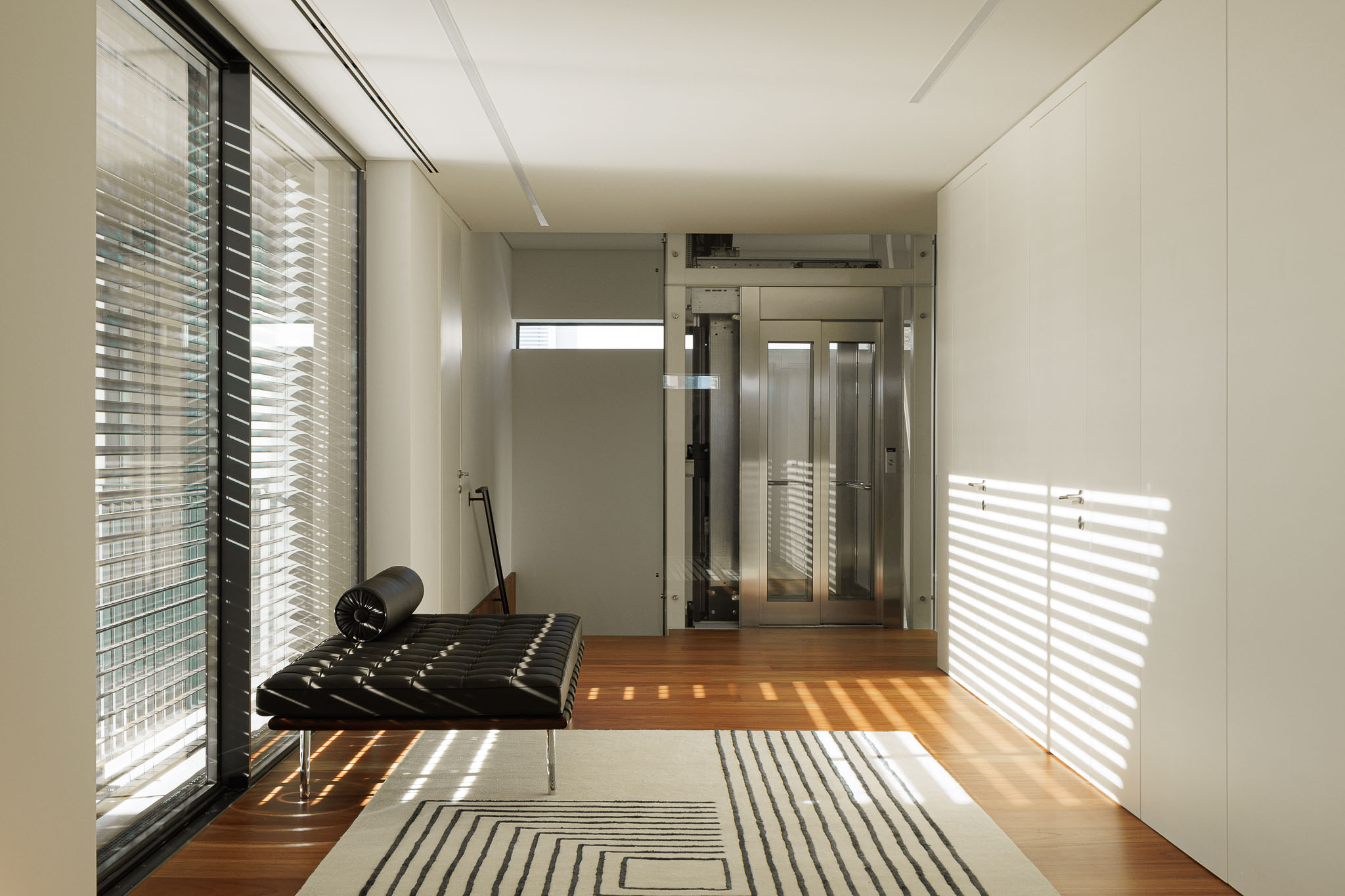 Hall de entrada: Banco de couro, elevador, armários embutidos e pavimento em madeira. — CONCRETE 11 arquitetura Cage Atelier em Lisboa