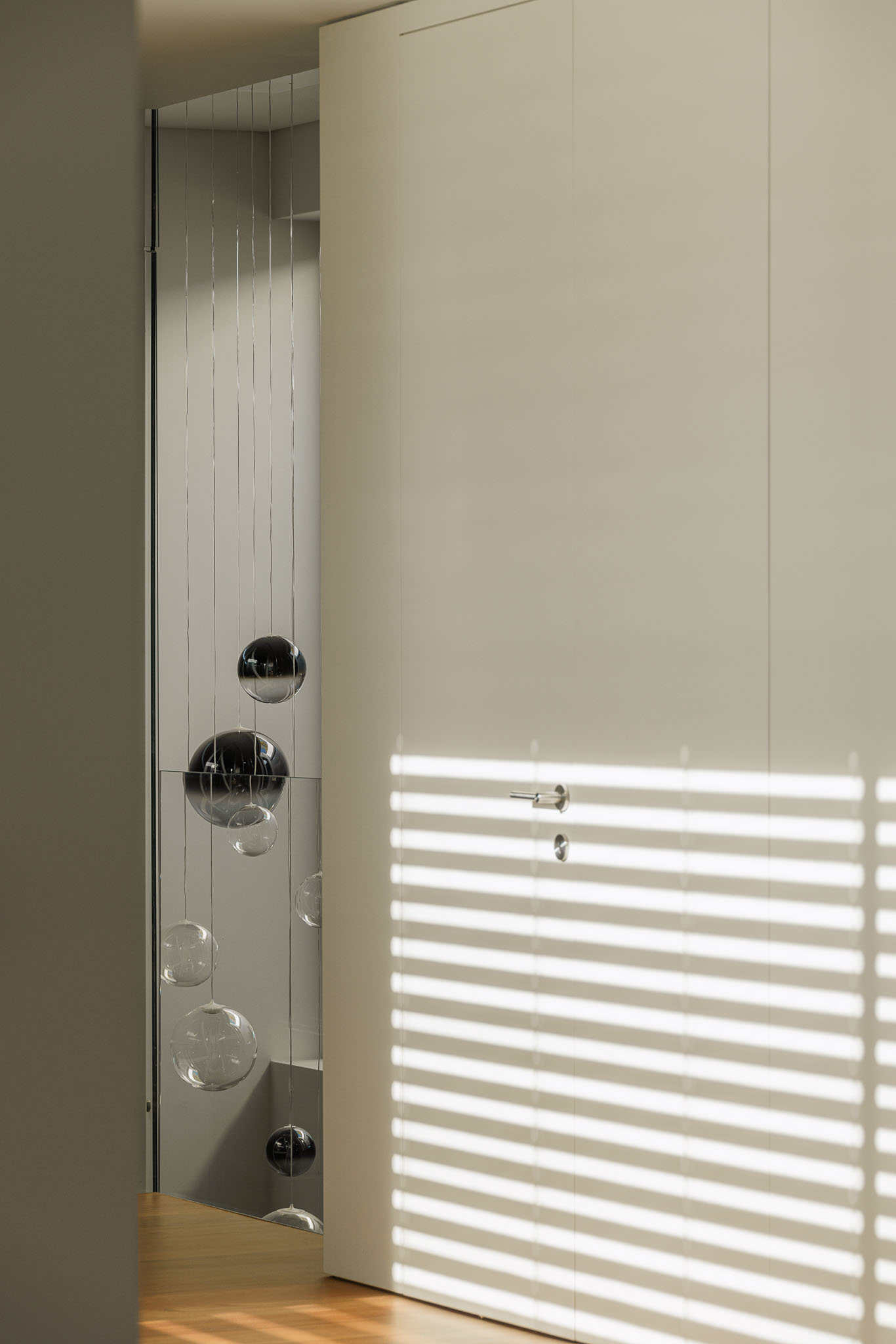 Hall de entrada: Candeeiro de teto com esferas de vidro, porta branca e luz natural filtrada por persianas. — CONCRETE 11 arquitetura Cage Atelier em Lisboa