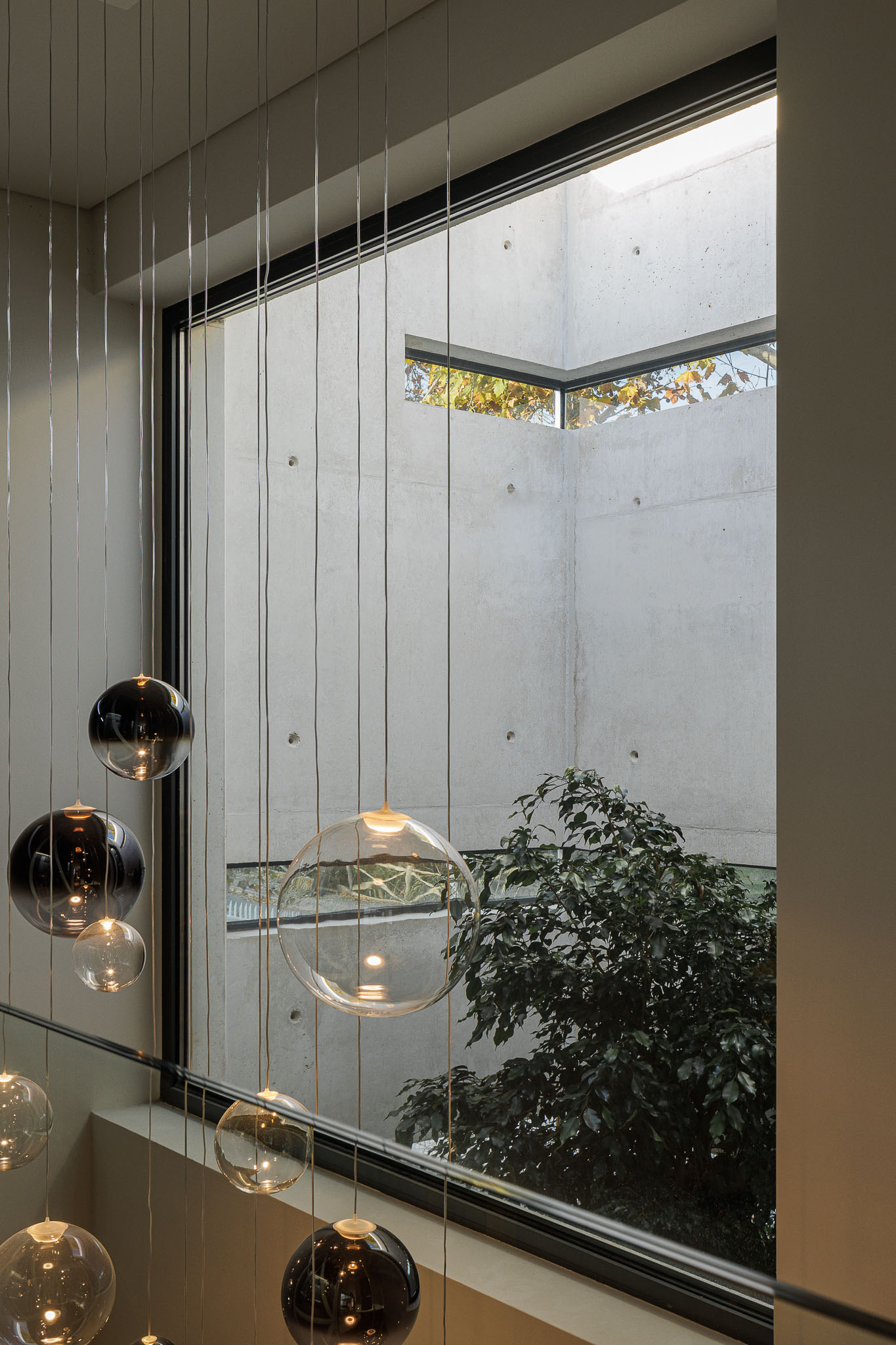 Hall de entrada: Candeeiro de teto com esferas de vidro e vista para o pátio interior com vegetação. — CONCRETE 11 arquitetura Cage Atelier em Lisboa
