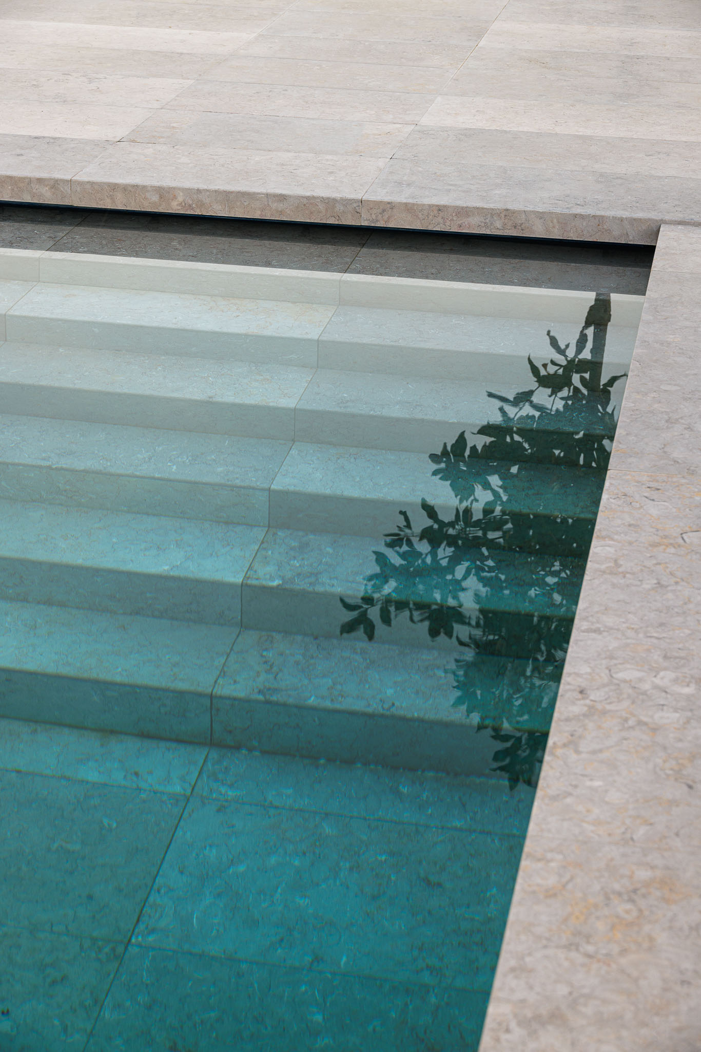 Piscina: Detalhe dos degraus de acesso à piscina com água cristalina e revestimento em pedra. — CONCRETE 11 arquitetura Cage Atelier em Lisboa