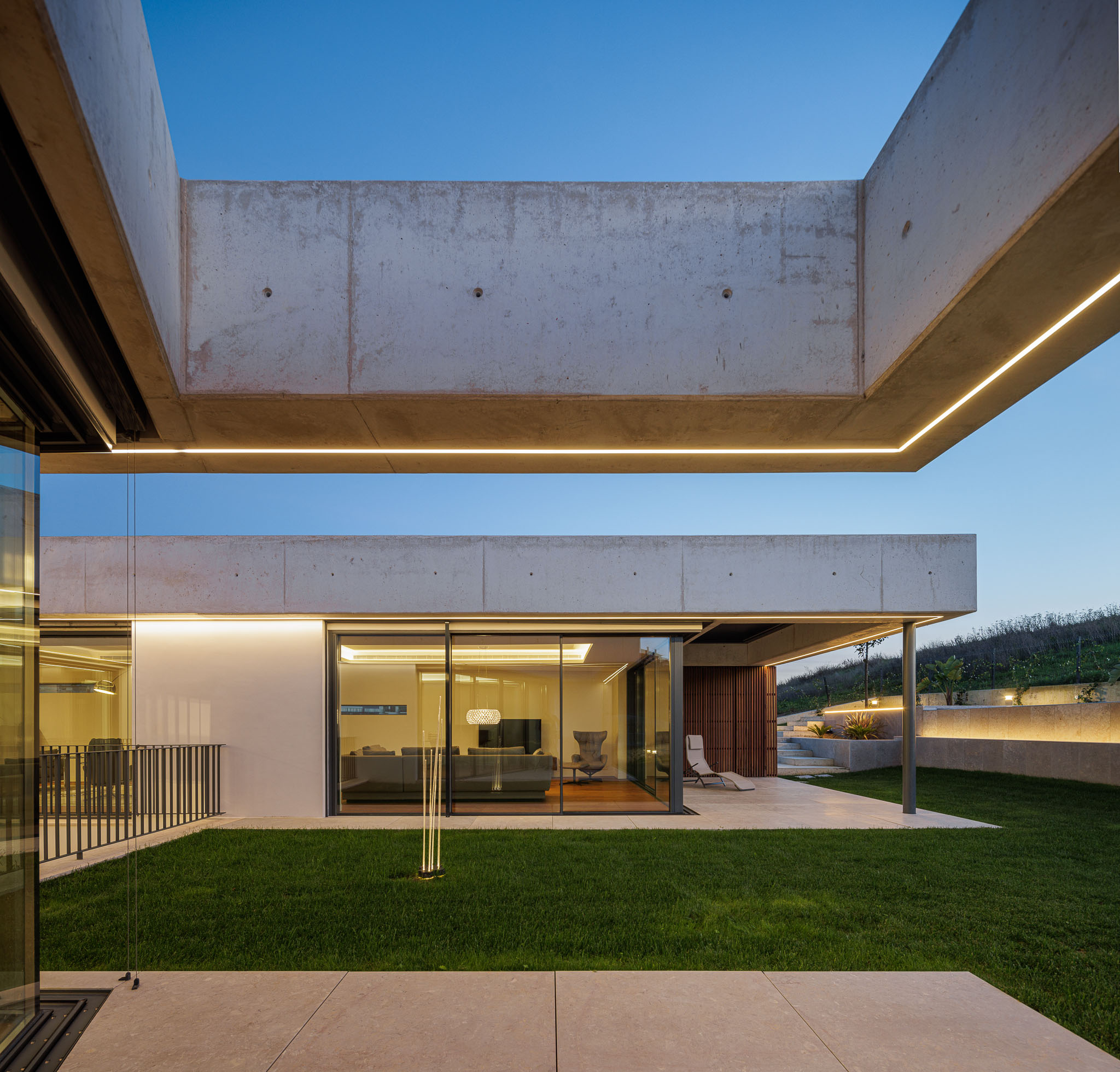 Exterior: Moradia moderna com iluminação exterior, jardim relvado e vista para a paisagem. — CONCRETE 11 arquitetura Cage Atelier em Lisboa