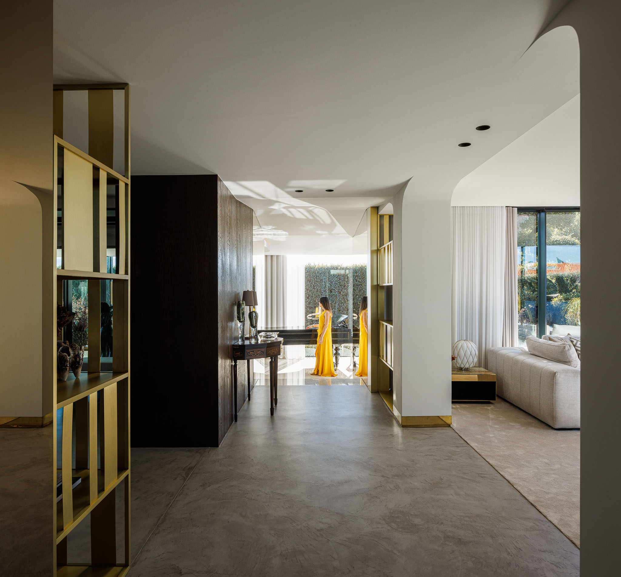 Hall: Espaço amplo com pavimento em microcimento, divisórias douradas e vista para a sala de estar e jantar. — Casa de Lavra arquitetura Ricardo Azevedo Arquitecto em Matosinhos