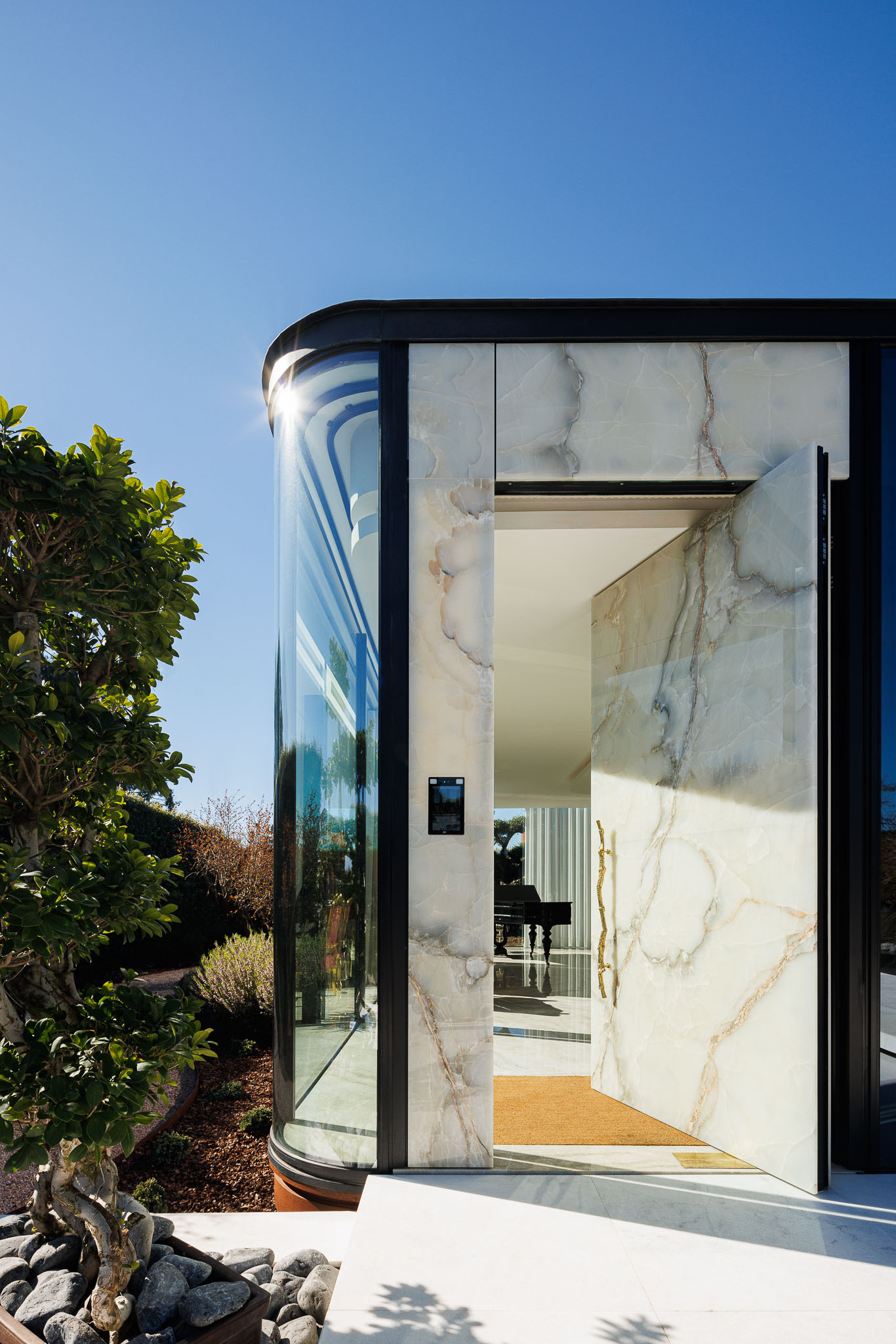 Entrada: Porta principal em ónix translúcido, com detalhes em metal preto, e vista para o interior da casa. — Casa de Lavra arquitetura Ricardo Azevedo Arquitecto em Matosinhos