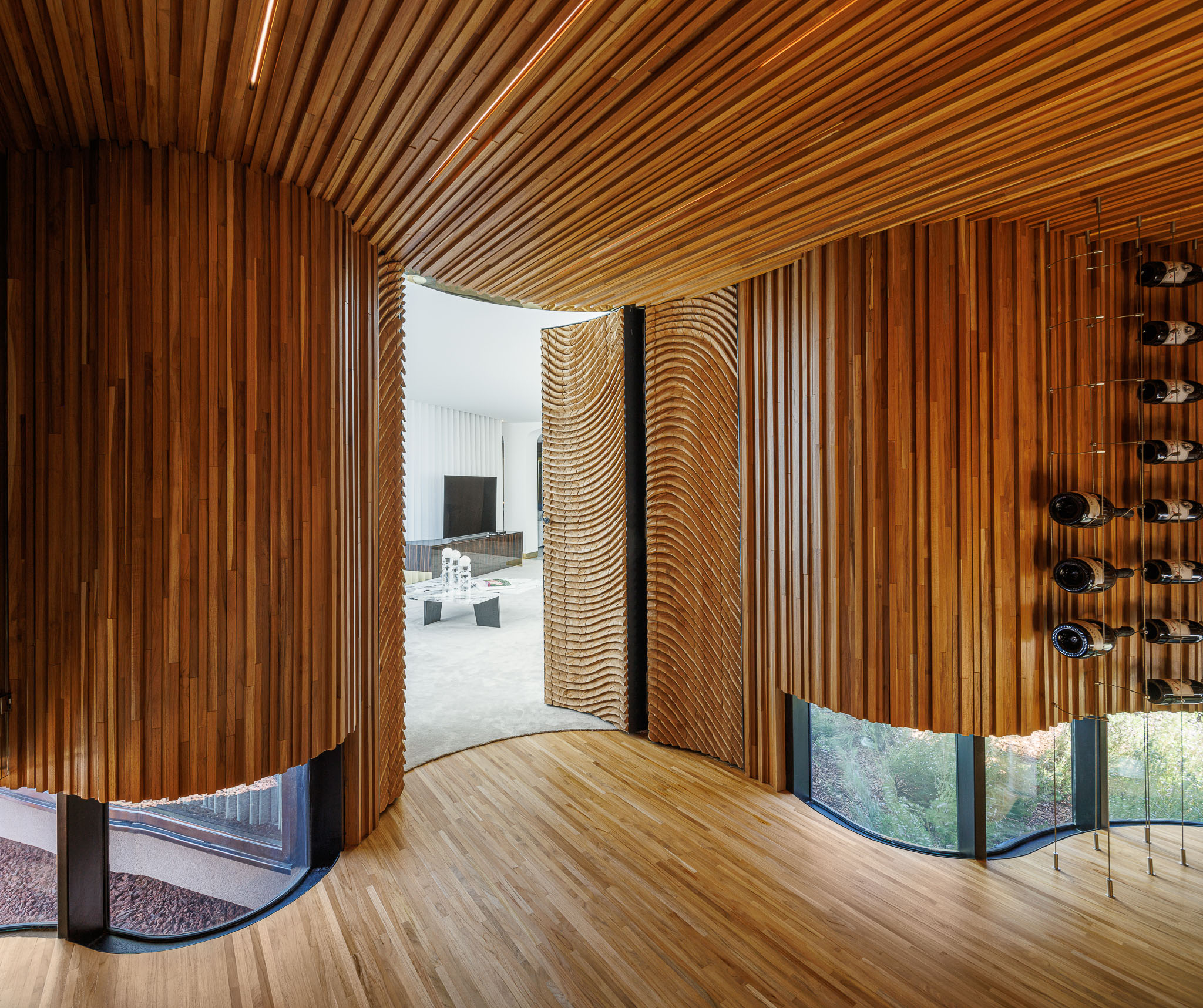 Adega: Espaço revestido em madeira com padrão ondulado, garrafeira metálica e vista para o exterior. — Casa de Lavra arquitetura Ricardo Azevedo Arquitecto em Matosinhos