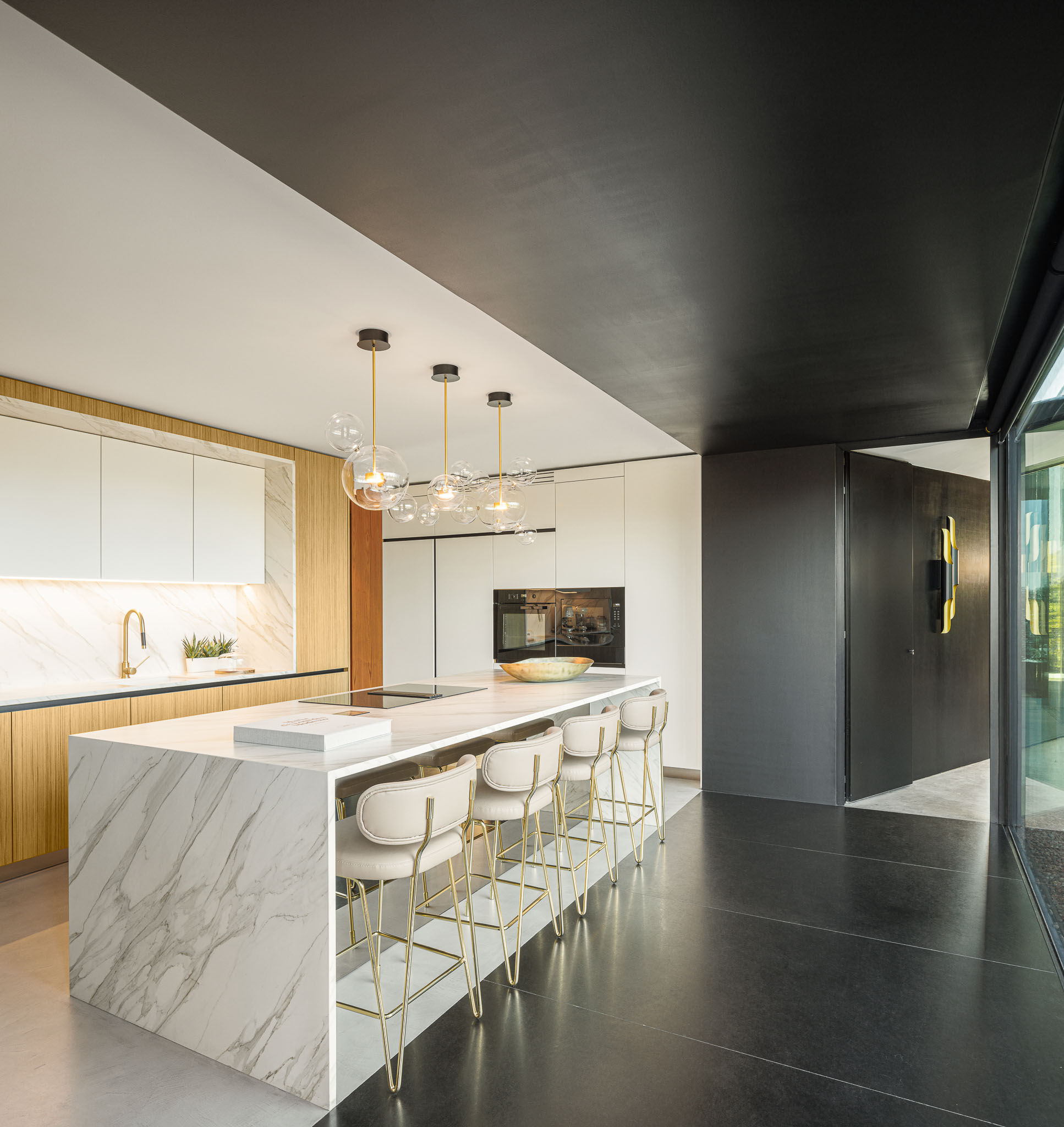Cozinha: Ilha central em mármore, armários brancos e em madeira, pavimento escuro e candeeiros suspensos. — Casa de Lavra arquitetura Ricardo Azevedo Arquitecto em Matosinhos
