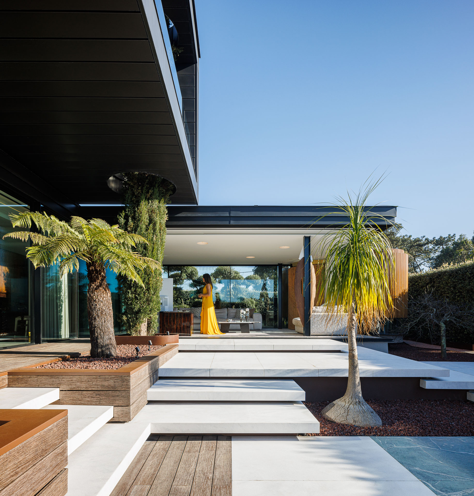 Exterior: Terraço com pavimento em pedra, jardim com palmeiras e vista para o interior da casa. — Casa de Lavra arquitetura Ricardo Azevedo Arquitecto em Matosinhos