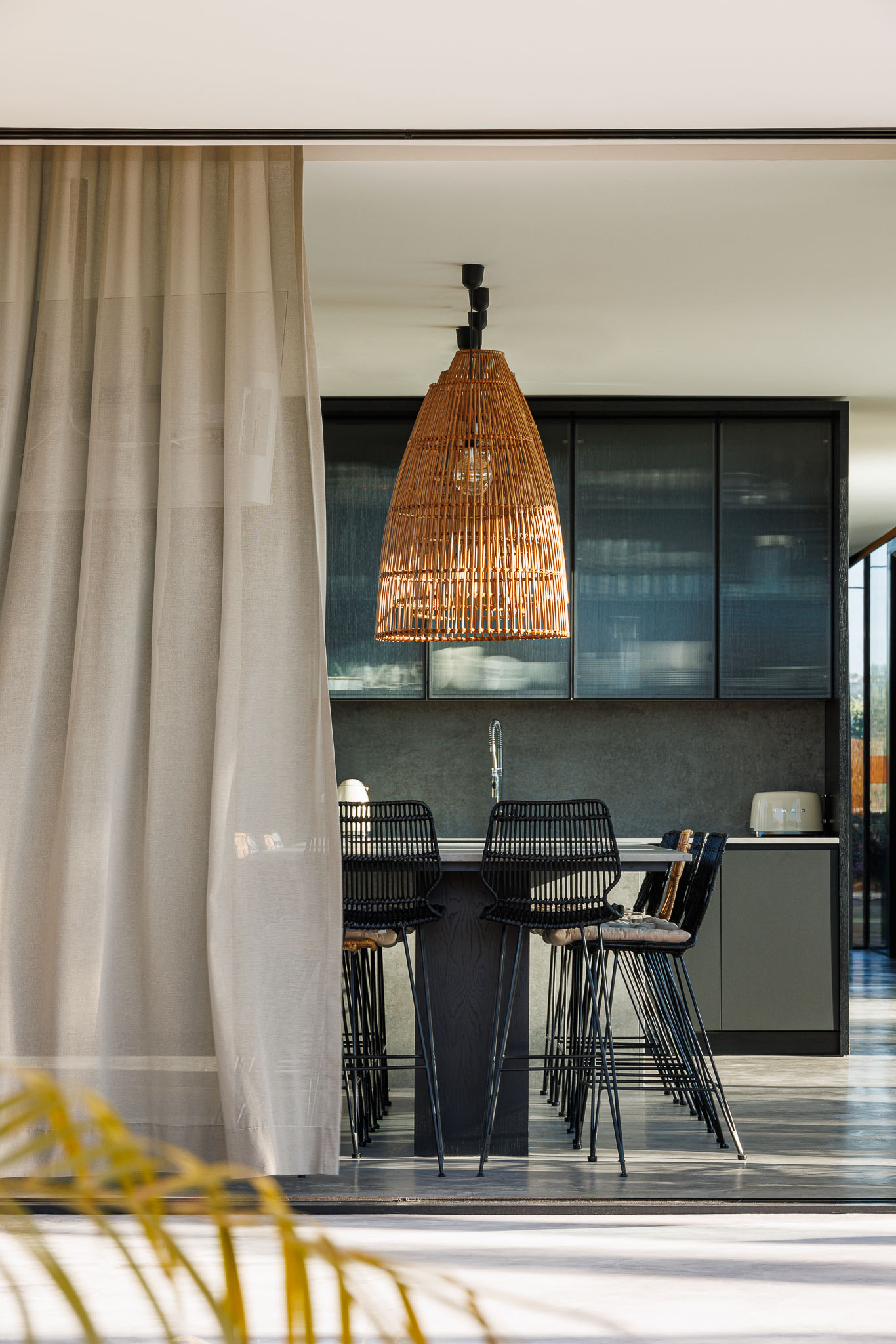Cozinha: Balcão com cadeiras altas, candeeiro de vime e armários escuros. — Casa de Lavra arquitetura Ricardo Azevedo Arquitecto em Matosinhos