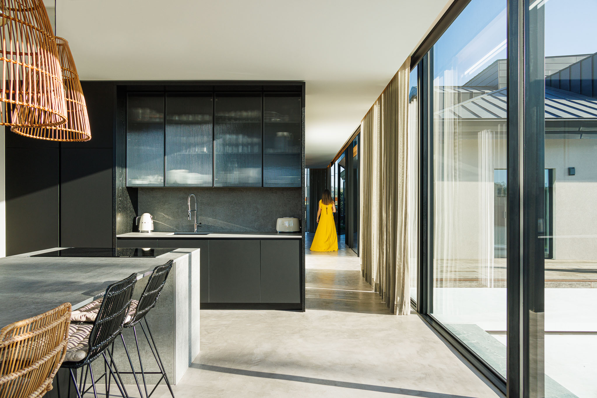 Cozinha: Armários escuros, balcão com cadeiras altas e candeeiros de vime. — Casa de Lavra arquitetura Ricardo Azevedo Arquitecto em Matosinhos