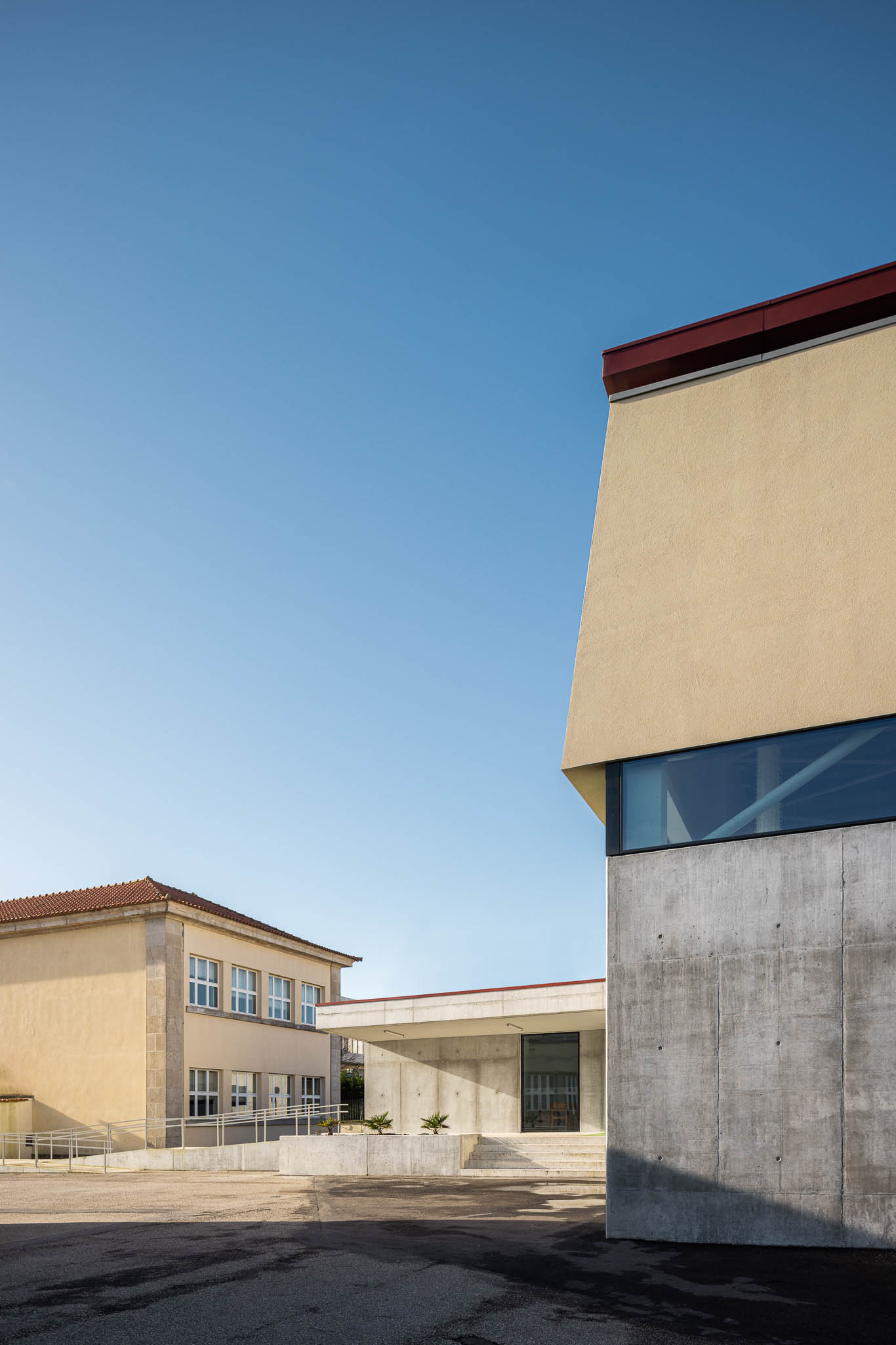 Fachada: Detalhe da fachada em betão e estuque amarelo, com janelas envidraçadas. — Pavilhão Desportivo da Escola Secundária Eça de Queirós arquitetura Oval em Póvoa de Varzim