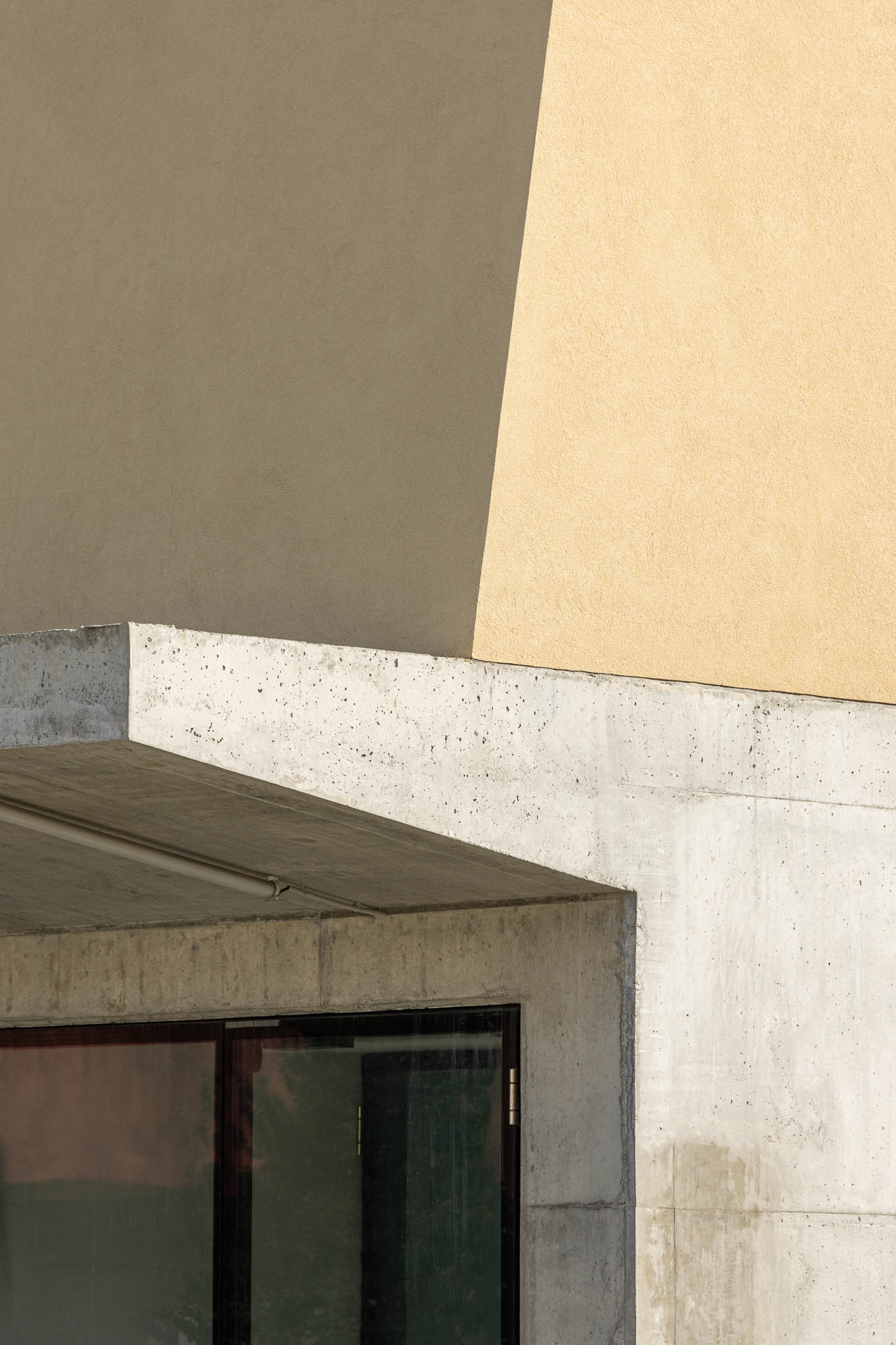 Fachada: Detalhe da esquina do edifício, com betão aparente e estuque amarelo. — Pavilhão Desportivo da Escola Secundária Eça de Queirós arquitetura Oval em Póvoa de Varzim