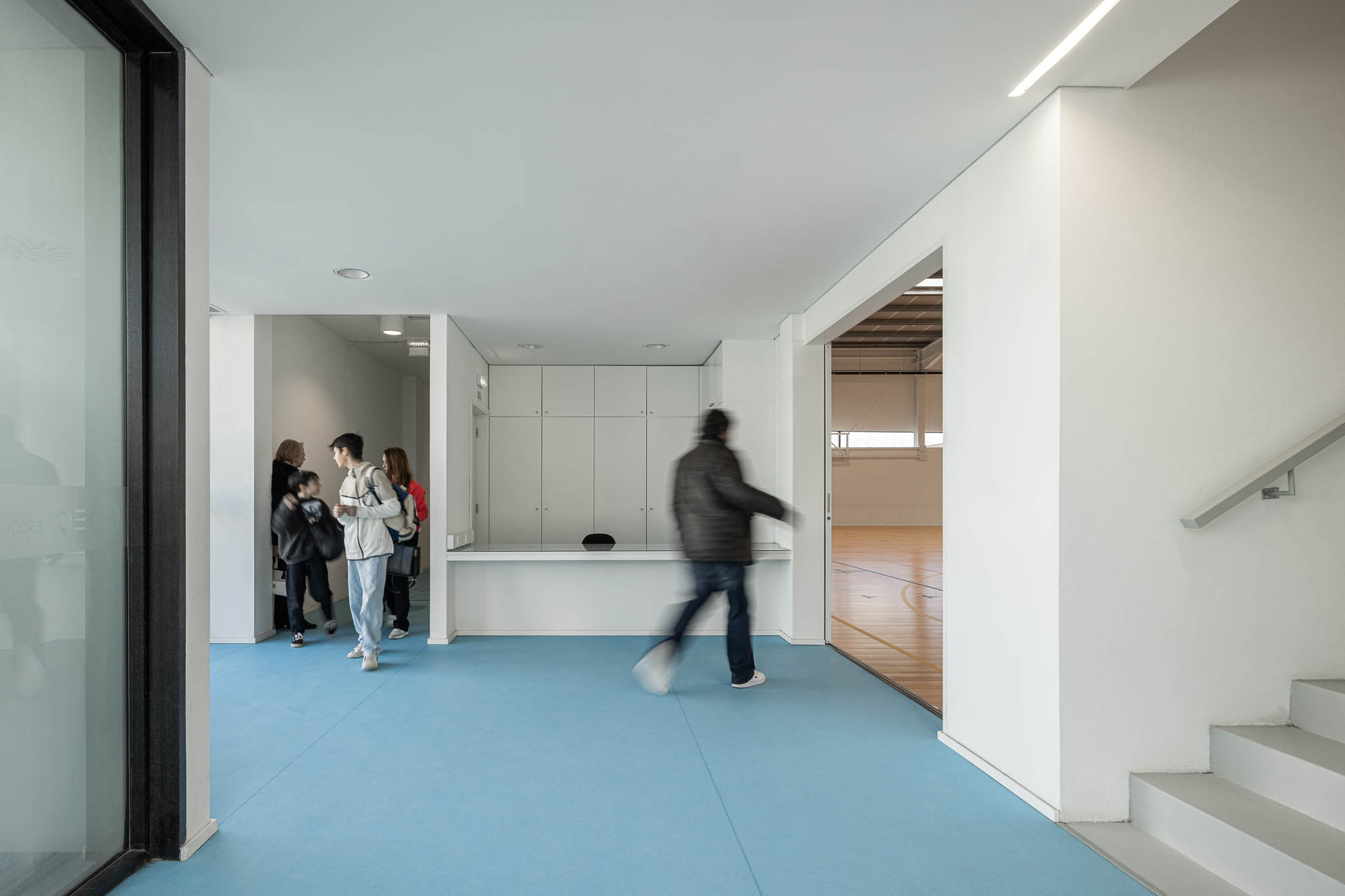 Hall: Hall de entrada com pavimento azul, balcão branco e acesso ao pavilhão. — Pavilhão Desportivo da Escola Secundária Eça de Queirós arquitetura Oval em Póvoa de Varzim