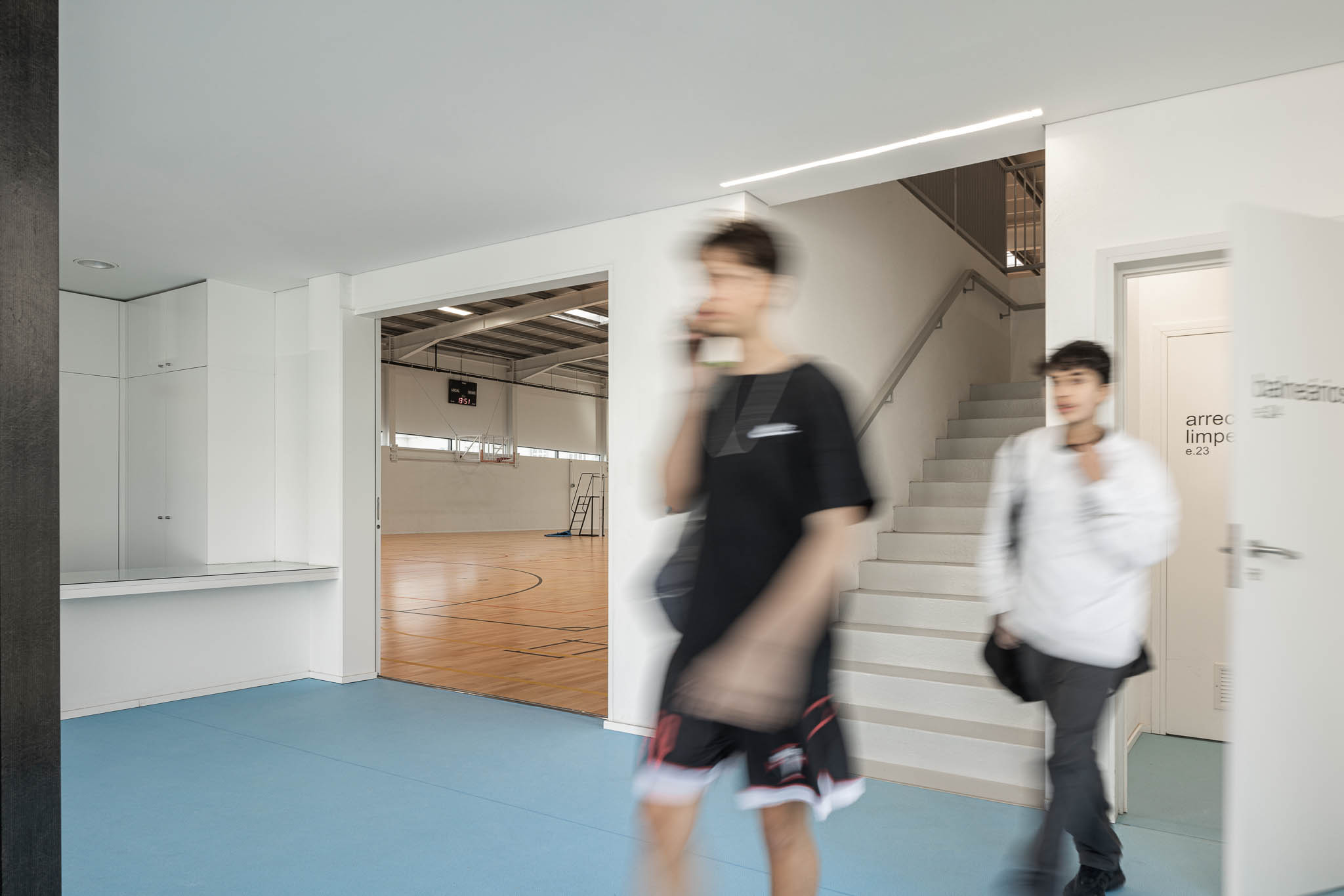 Hall: Corredor com pavimento azul, acesso ao pavilhão e escadas para o piso superior. — Pavilhão Desportivo da Escola Secundária Eça de Queirós arquitetura Oval em Póvoa de Varzim