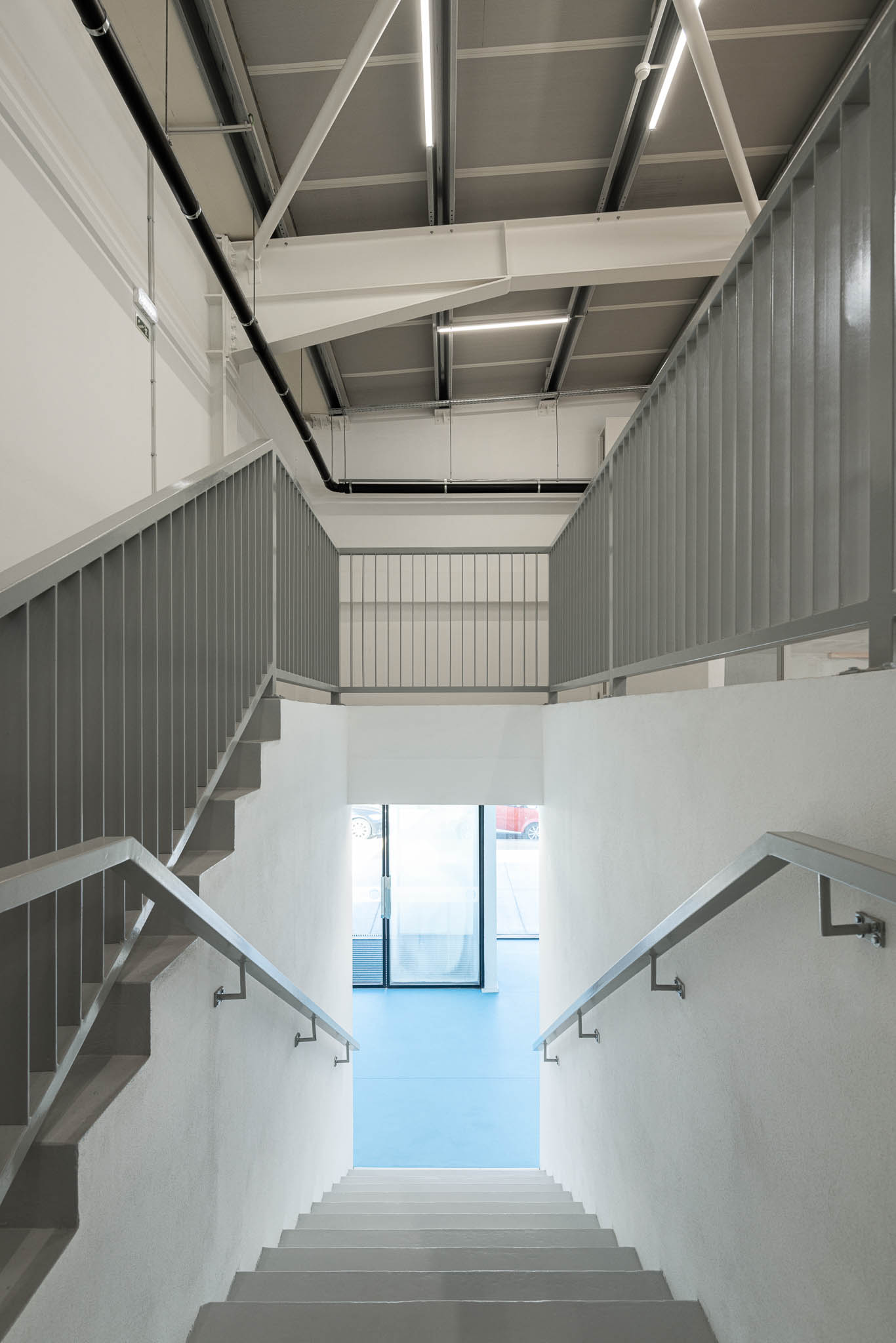 Escadas: Escadas em betão branco com corrimão metálico, pavimento azul no patamar inferior. — Pavilhão Desportivo da Escola Secundária Eça de Queirós arquitetura Oval em Póvoa de Varzim