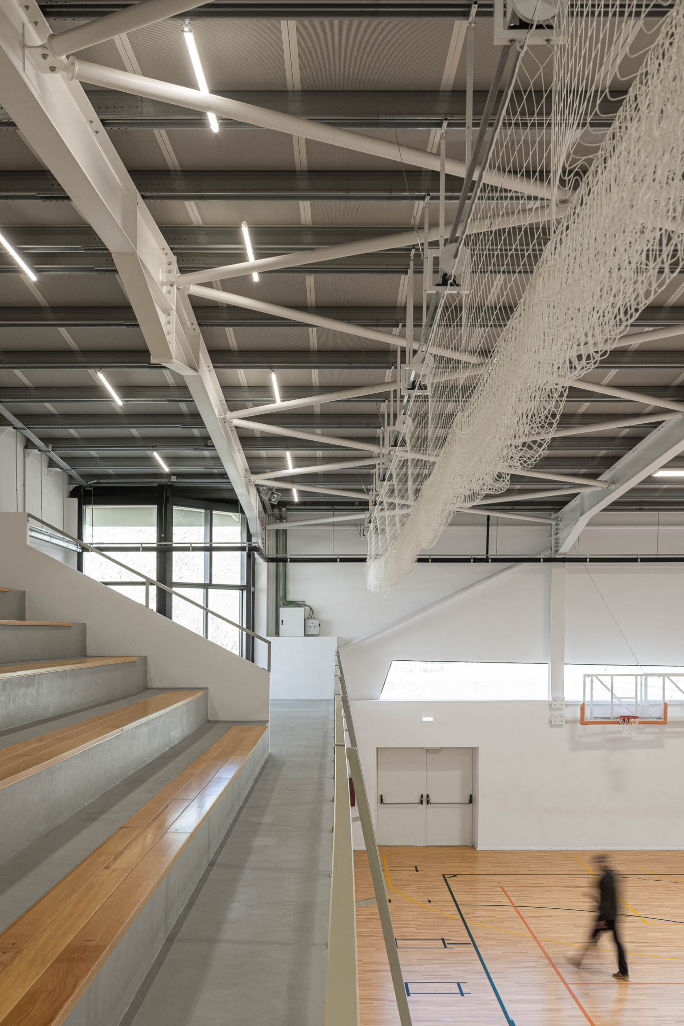 Bancada: Vista da bancada superior com assentos em madeira, estrutura metálica no teto. — Pavilhão Desportivo da Escola Secundária Eça de Queirós arquitetura Oval em Póvoa de Varzim