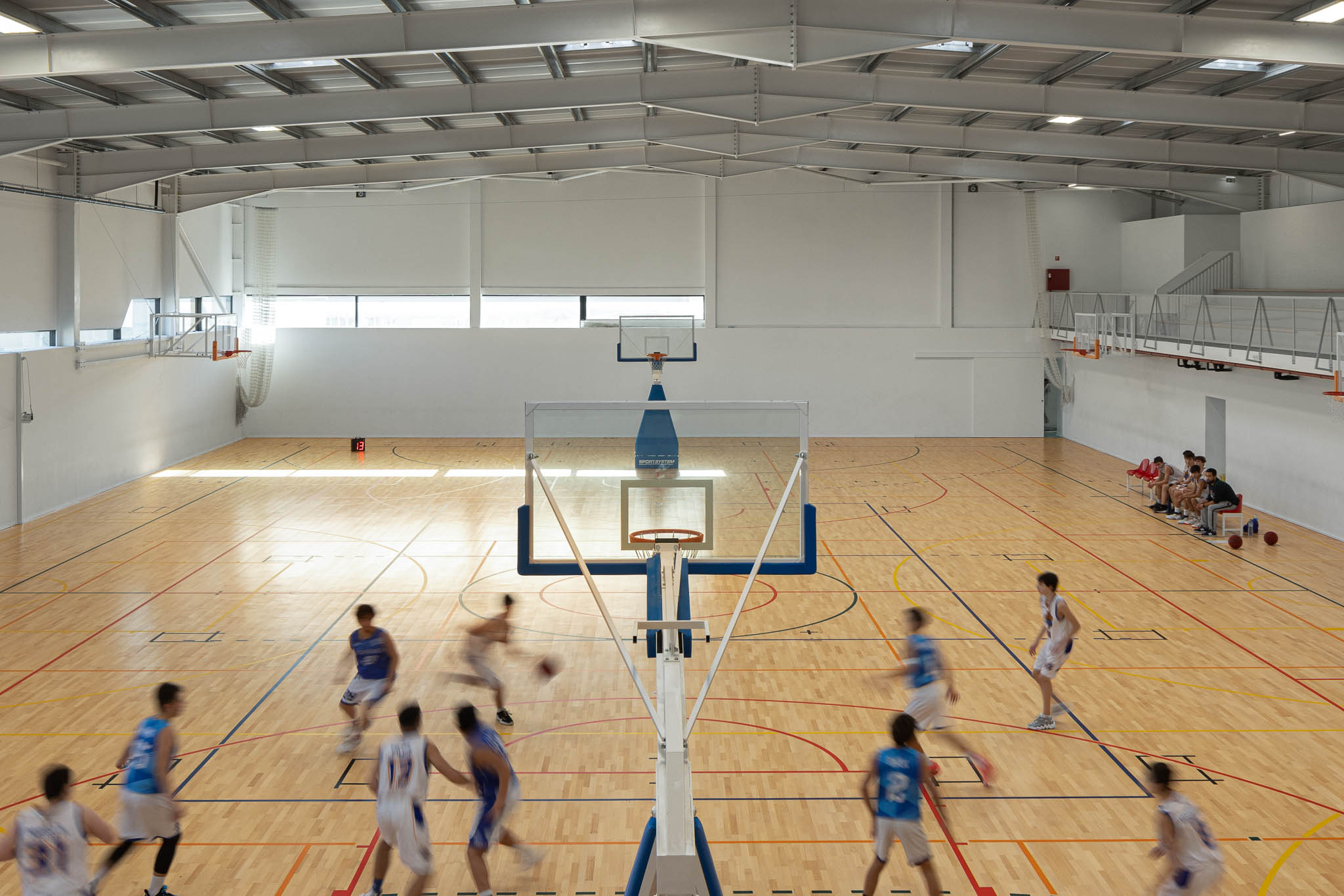 Pavilhão: Vista ampla do pavilhão com campo de jogos, bancadas e estrutura metálica exposta. — Pavilhão Desportivo da Escola Secundária Eça de Queirós arquitetura Oval em Póvoa de Varzim