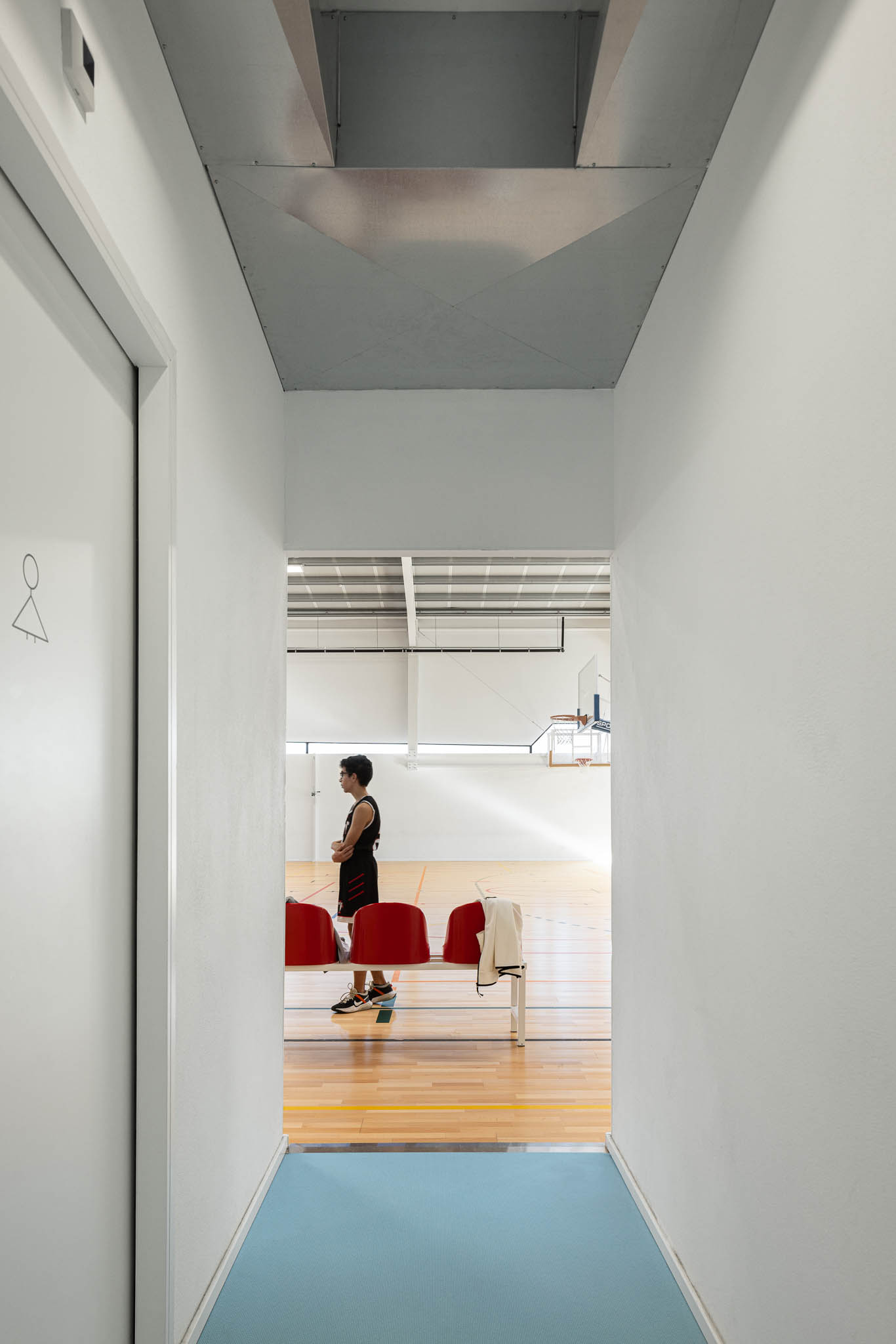 Corredor: Corredor com pavimento azul, portas para os balneários e iluminação linear. — Pavilhão Desportivo da Escola Secundária Eça de Queirós arquitetura Oval em Póvoa de Varzim
