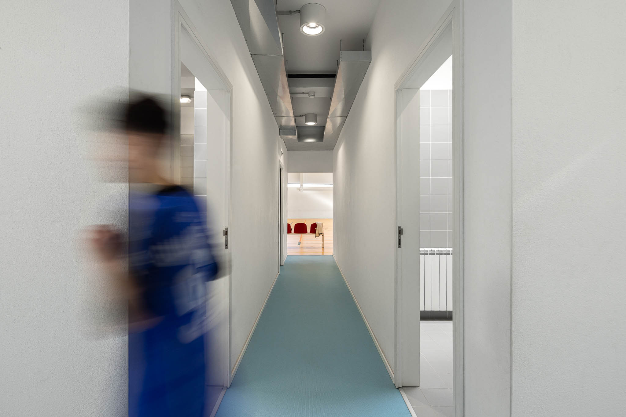 Corredor: Corredor longo com pavimento azul, portas para os balneários e iluminação embutida. — Pavilhão Desportivo da Escola Secundária Eça de Queirós arquitetura Oval em Póvoa de Varzim