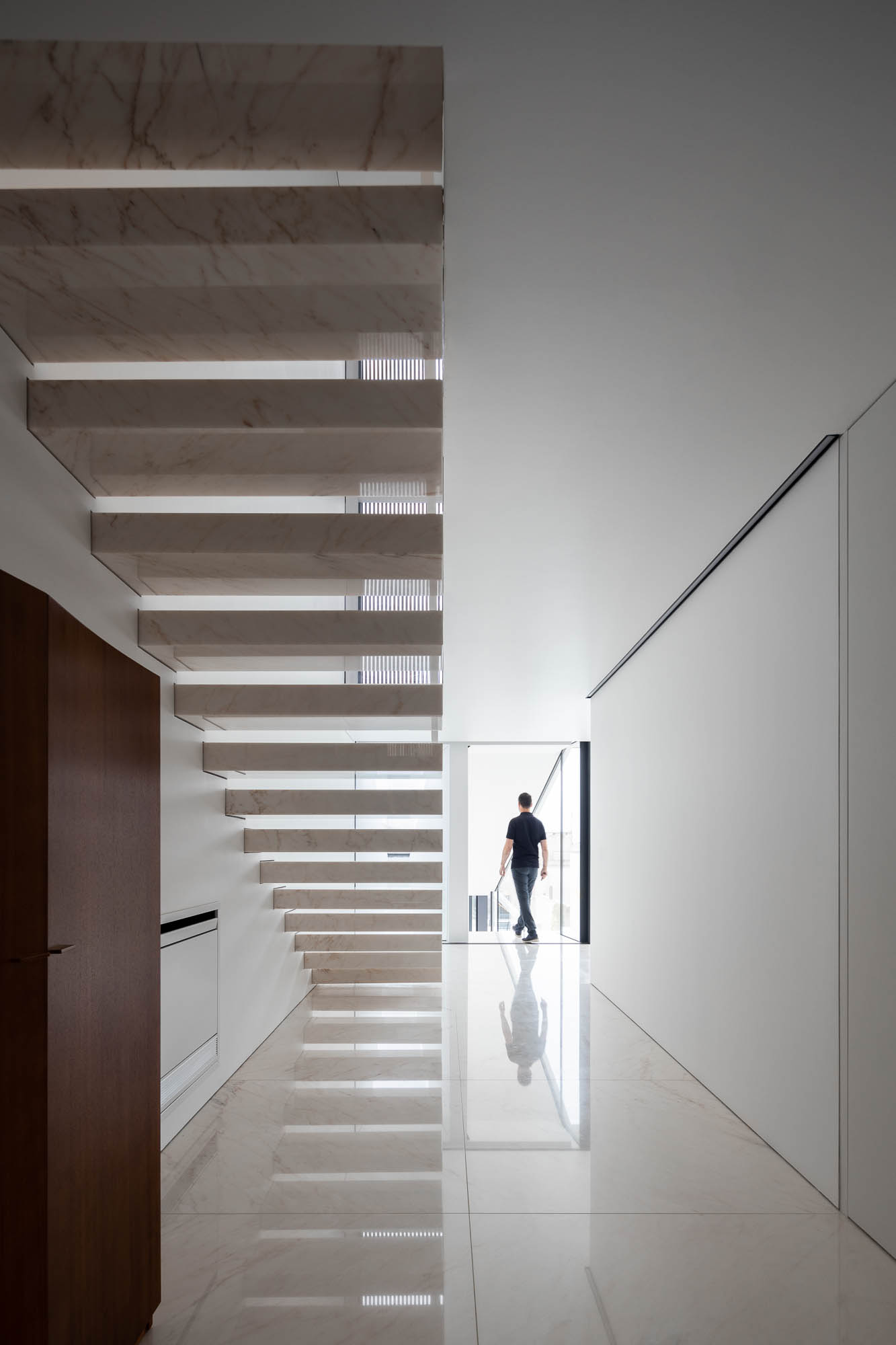 Corredor: Escadas flutuantes em mármore branco, pavimento brilhante, paredes brancas e porta em madeira escura. Estilo minimalista. — Casa Costa Nova arquitetura Espaço Objecto em Ílhavo